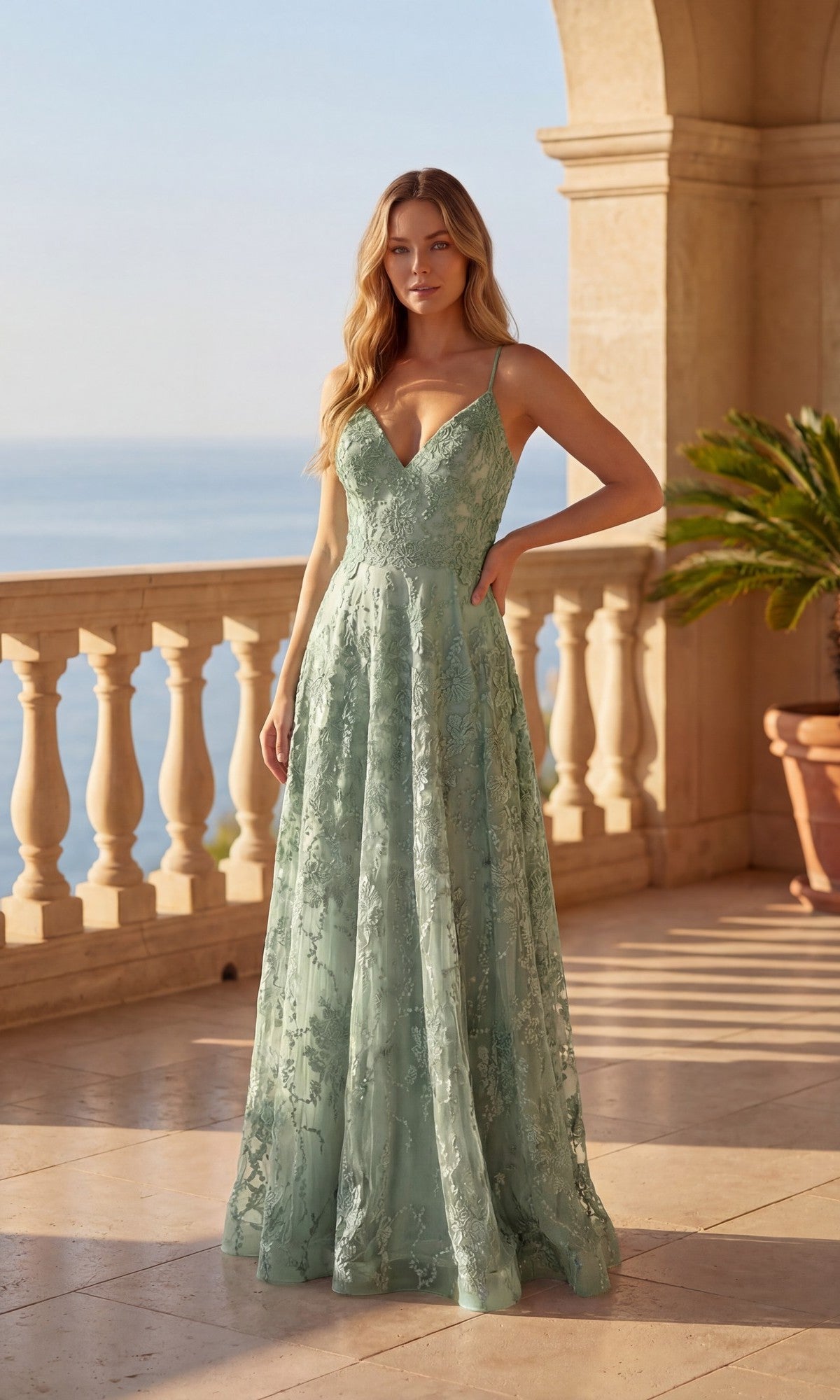 A woman in the Chicas C804 long prom dress in sage, featuring a V-neck and lace-up back, stands on a stone terrace with balustrades overlooking the sea.