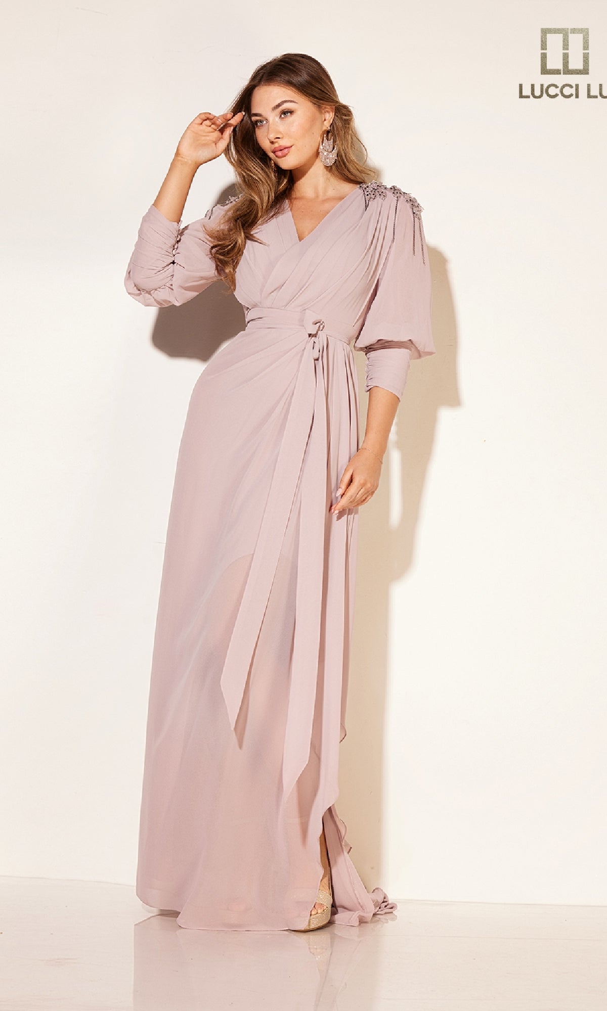 A woman models the Lucci Lu C8092 long formal dress in light mauve, featuring a wrap design, long sleeves, and tied waist, standing against a plain white background.