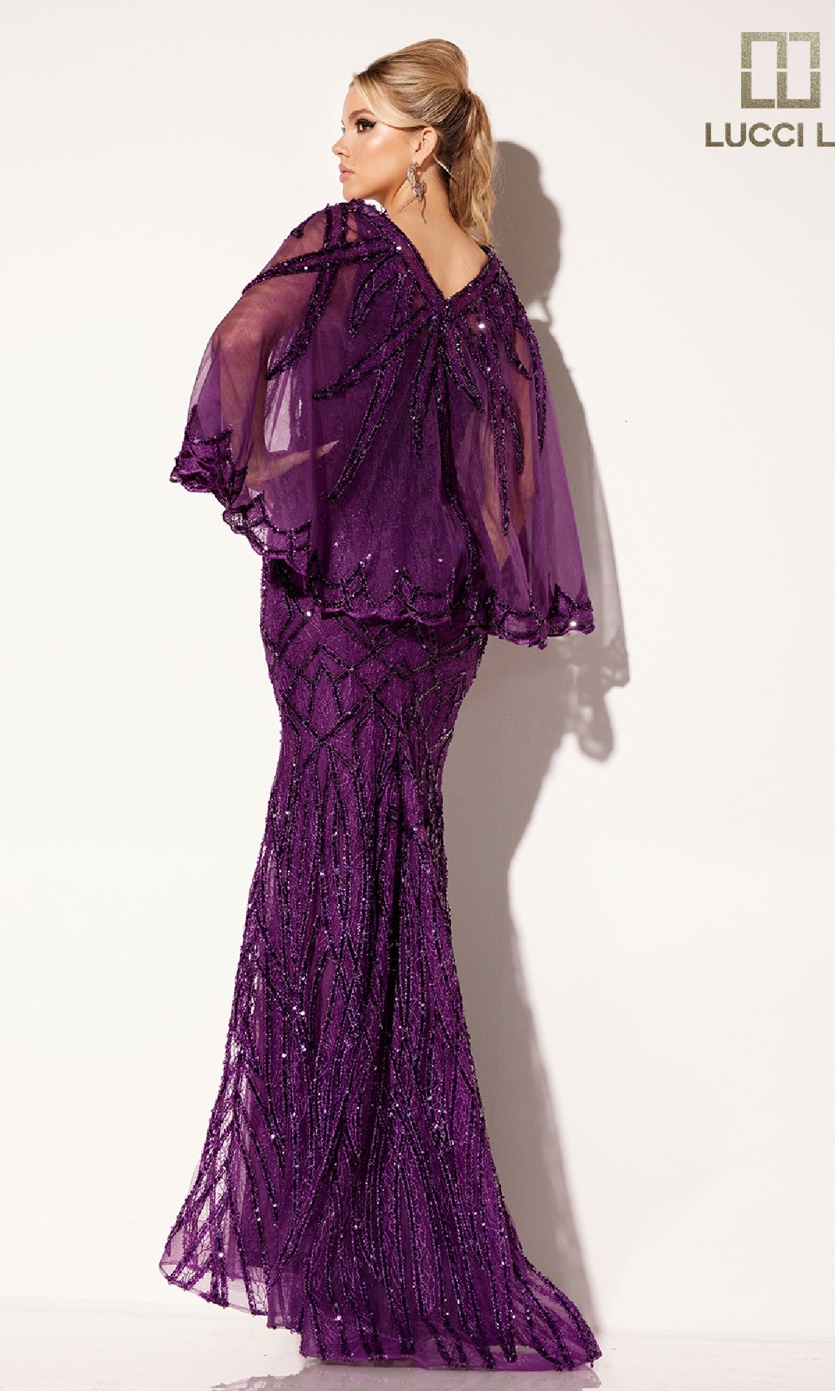 A woman models the Lucci Lu C8109 long formal dress, a fitted purple gown with beaded patterns and a sheer capelet, flowing elegantly to the floor as she faces away from the camera.