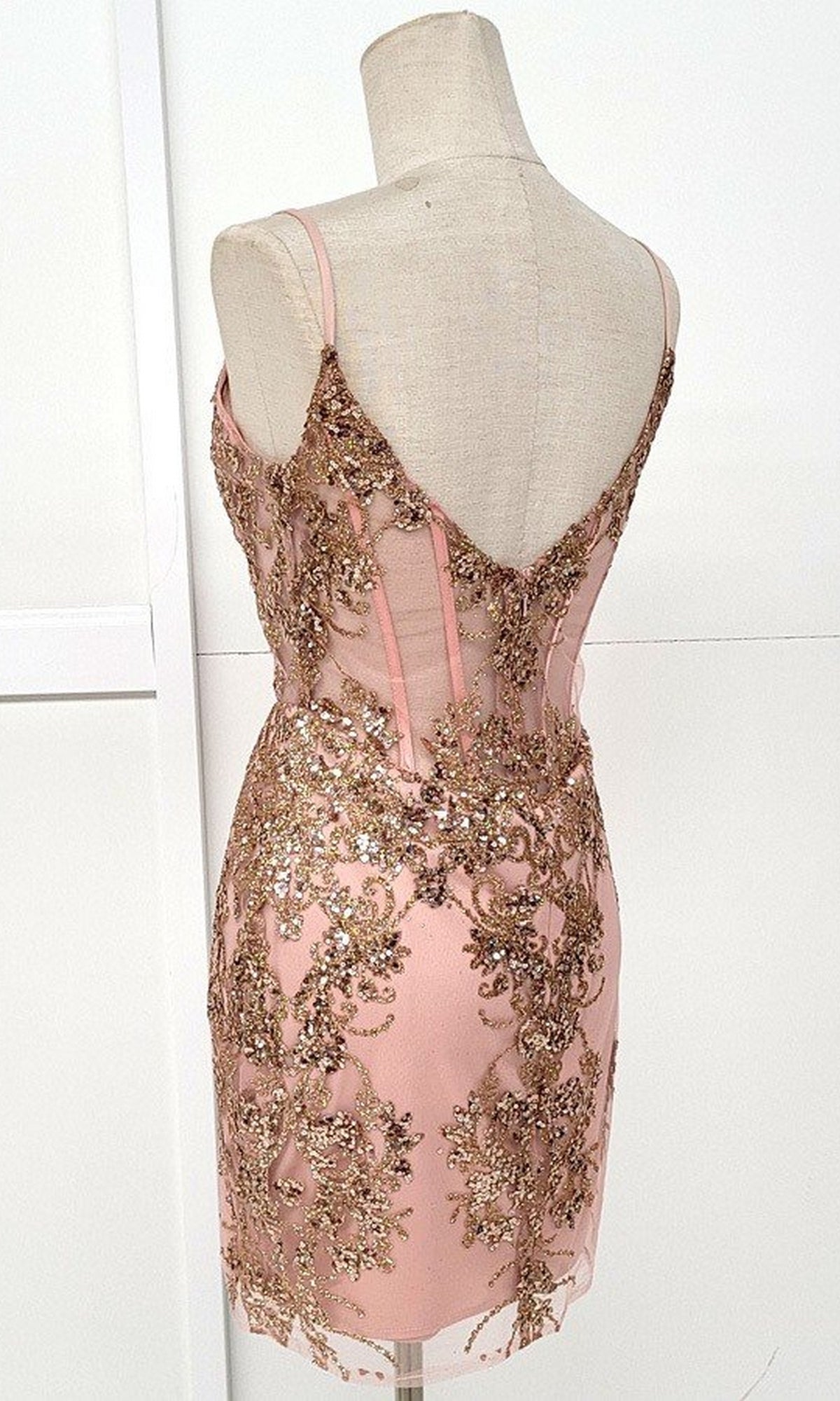 A back view of the Sheer-Corset Short Glitter Homecoming Dress C814 in light pink, sleeveless with gold sequin embroidery, glitter print, and a low V-shaped back on a mannequin.