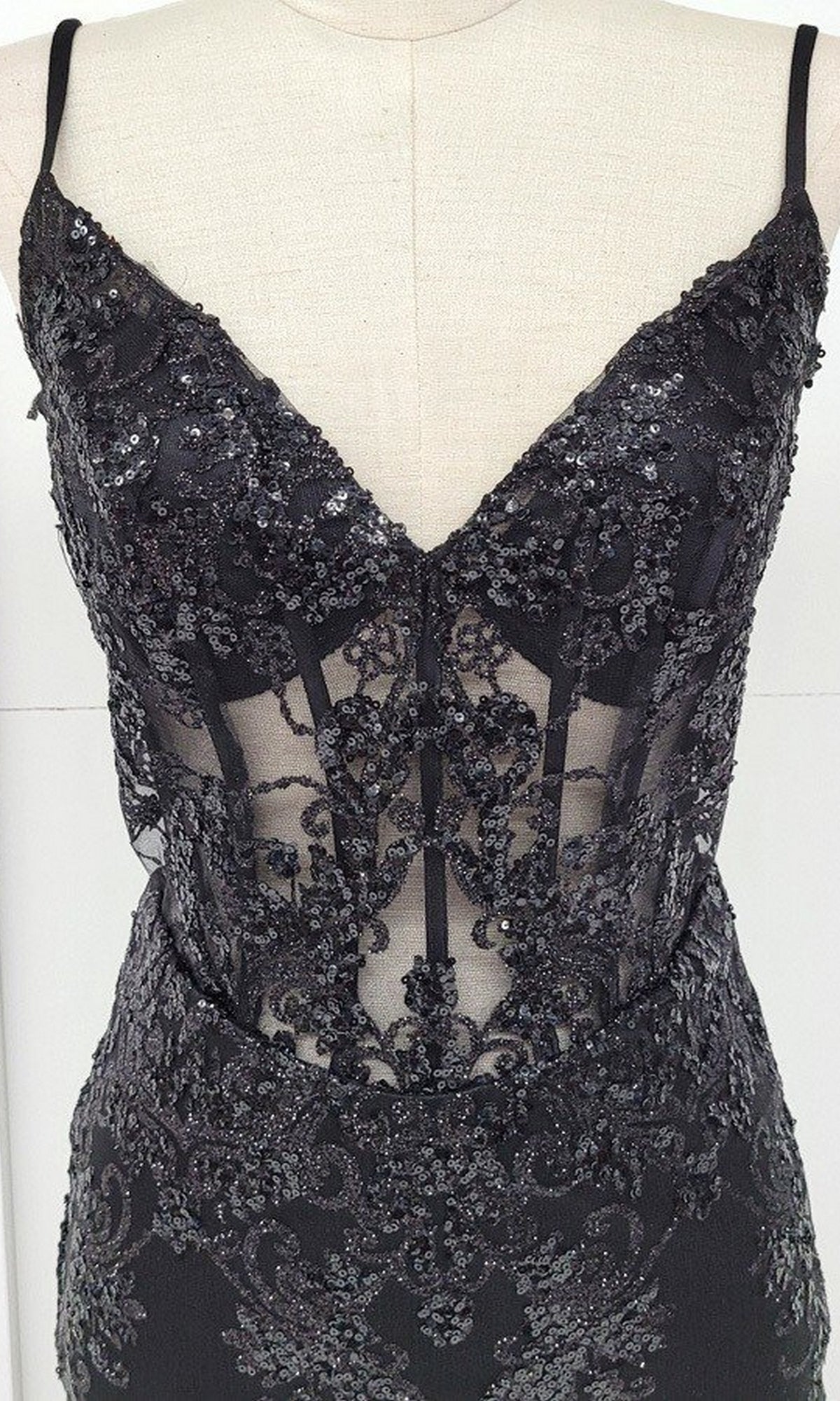 The Sheer-Corset Short Glitter Homecoming Dress C814 is a sleeveless black evening dress with a deep V-neckline, sheer corset-style panels, and detailed sequin and lace embellishments shown on a mannequin.