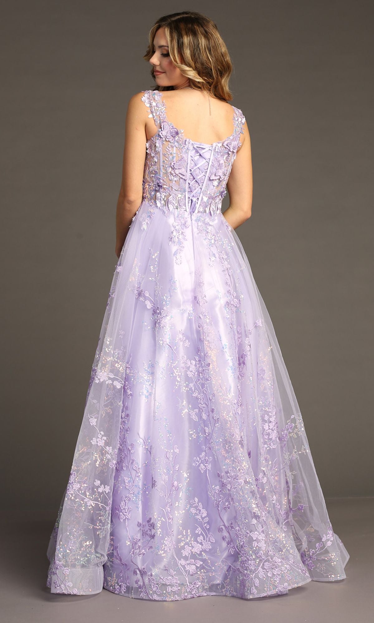 A woman faces away in a Floral-Print Lace-Up Long Prom Dress: Chicas C818, showcasing light purple fabric with floral embroidery, a corset-style bodice, and lace-up back against a plain gray background.