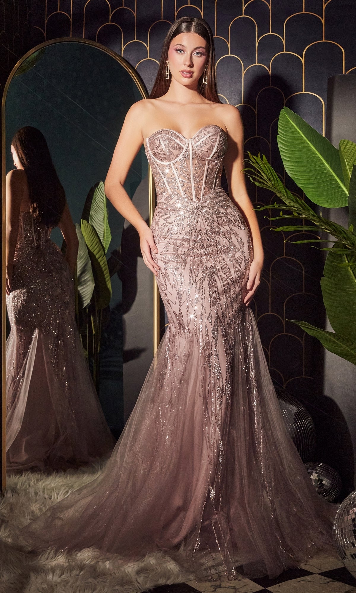 A woman in a Strapless Long Pink Mermaid Prom Dress CB116 stands before a mirror, surrounded by lush green plants and Art Deco decor.