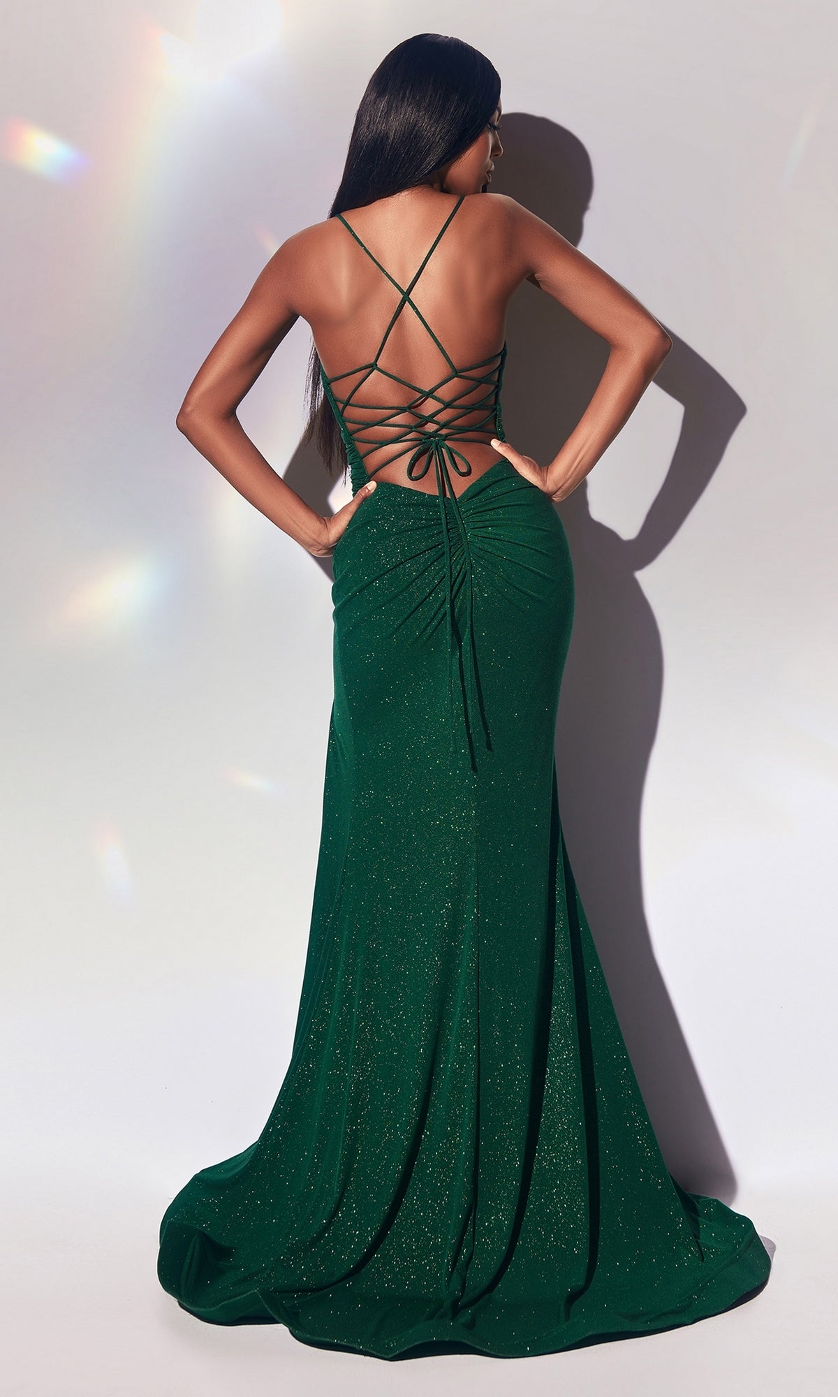 A woman faces away, wearing the Empire-Waist Long Glitter Prom Dress CC2162 in dark green, featuring thin straps, a lace-up open back, and a floor-length hem.