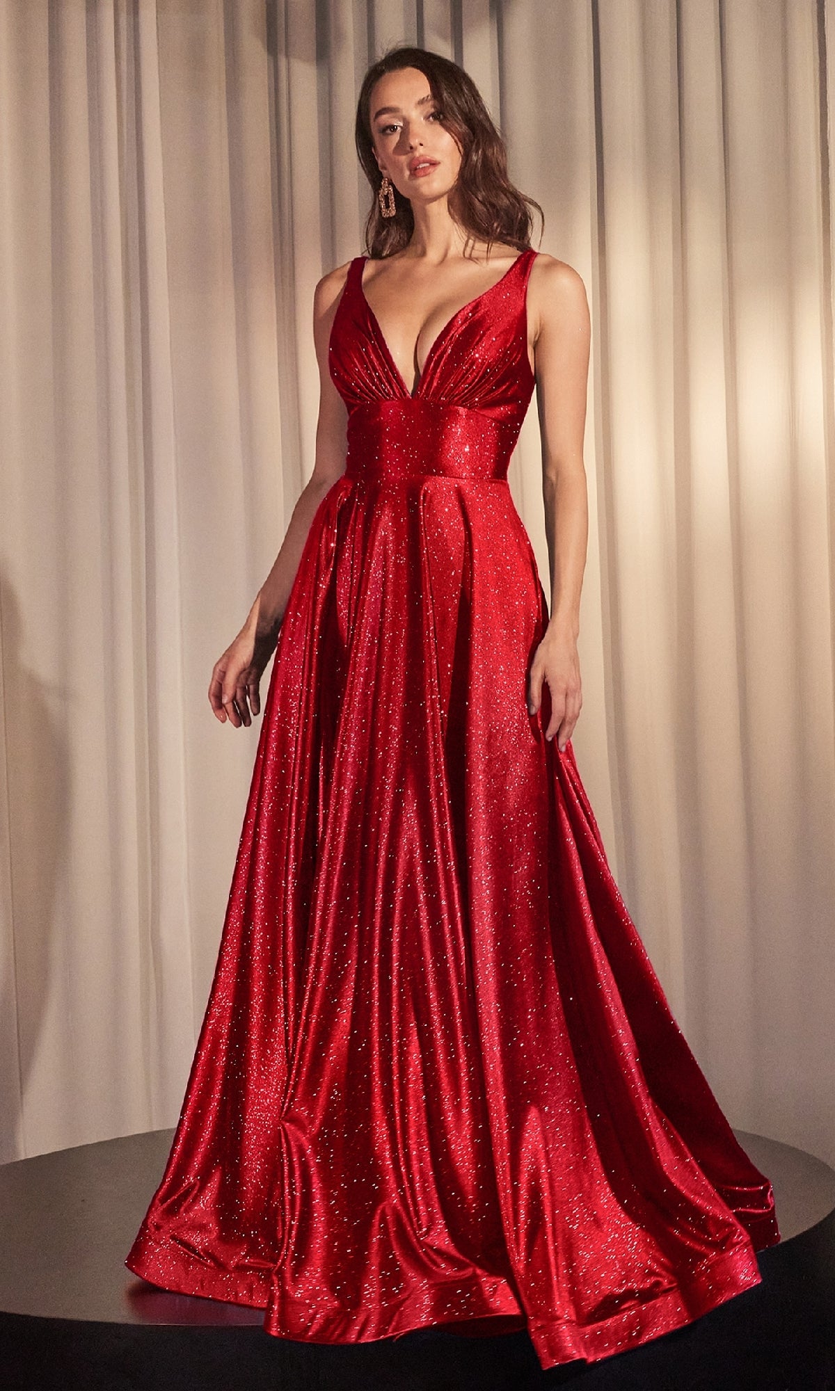 Woman wearing the Ladivine CC2349—a V-neck, sleeveless, floor-length A-line glitter prom dress—stands before white curtains.