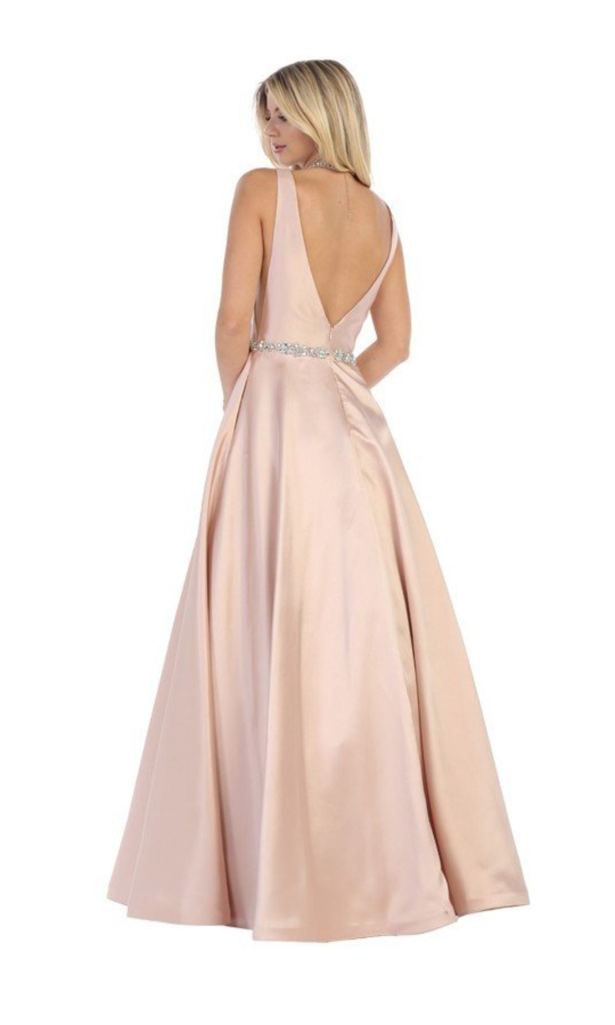 Woman in the Chicas CC3021 Jeweled-Waist Long Prom Ball Gown—sleeveless, floor-length, light pink satin A-line dress with a jeweled waistband and deep V-back—stands looking over her shoulder.