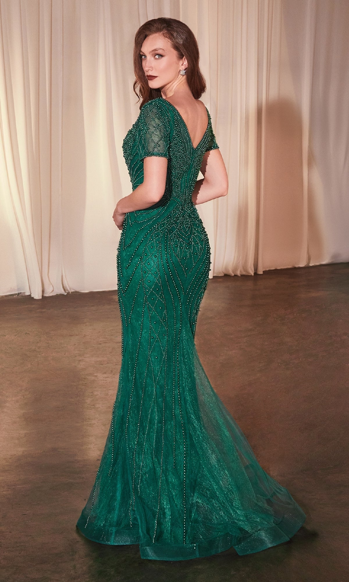 A woman stands gracefully in the Ladivine CC4019, a short-sleeve beaded formal dress, its elegant green fabric capturing the light beautifully.