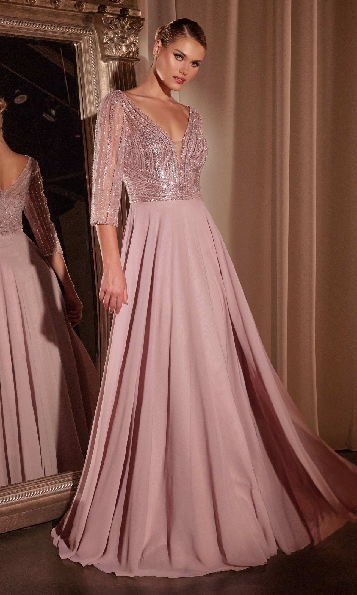 A woman stands before a mirror in the Ladivine CC446, a modest long A-line formal dress featuring a sequined bodice, sheer sleeves, and a flowing mauve skirt.