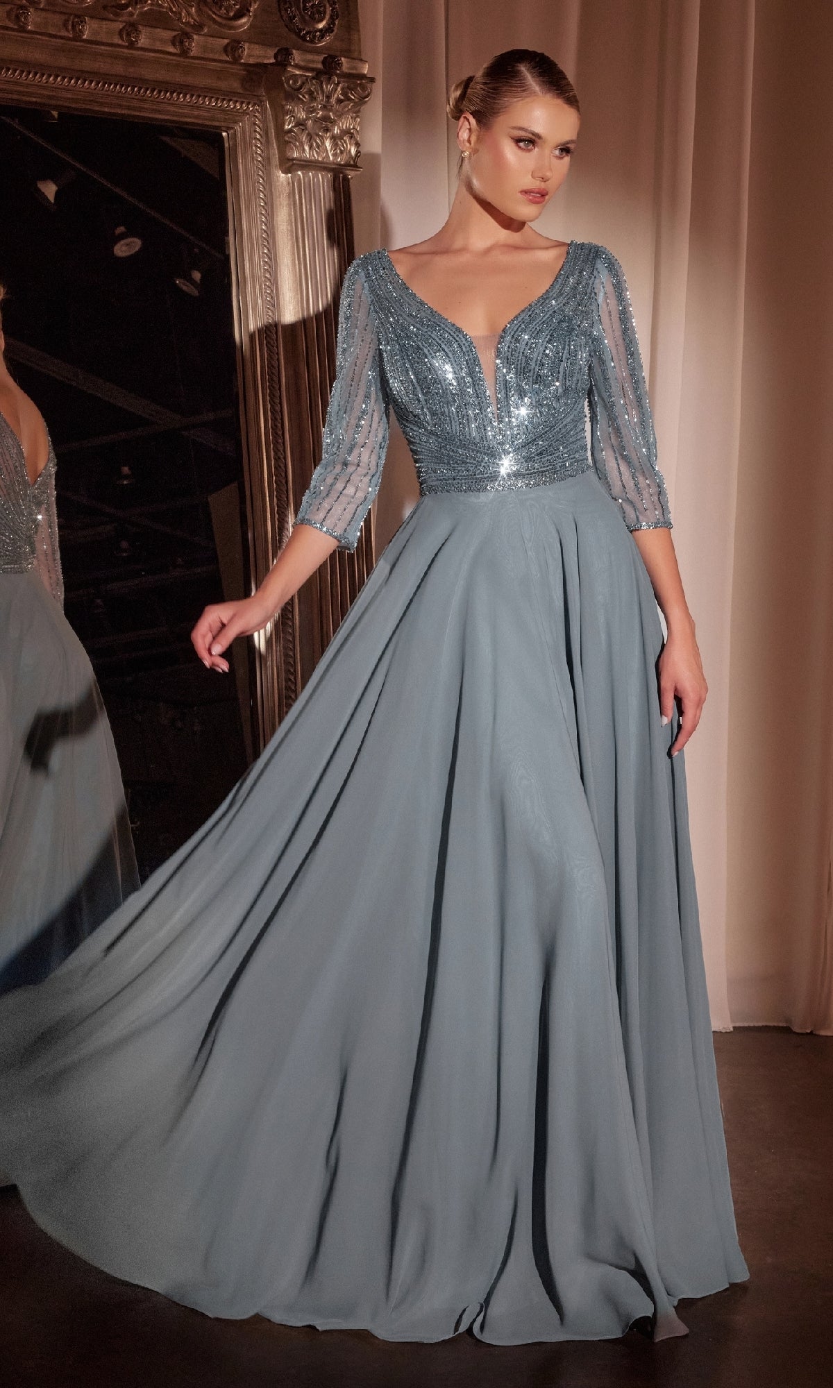 A woman stands before a grand mirror wearing the Ladivine CC446, a modest long A-line formal dress in light blue featuring a beaded bodice and sheer three-quarter sleeves.
