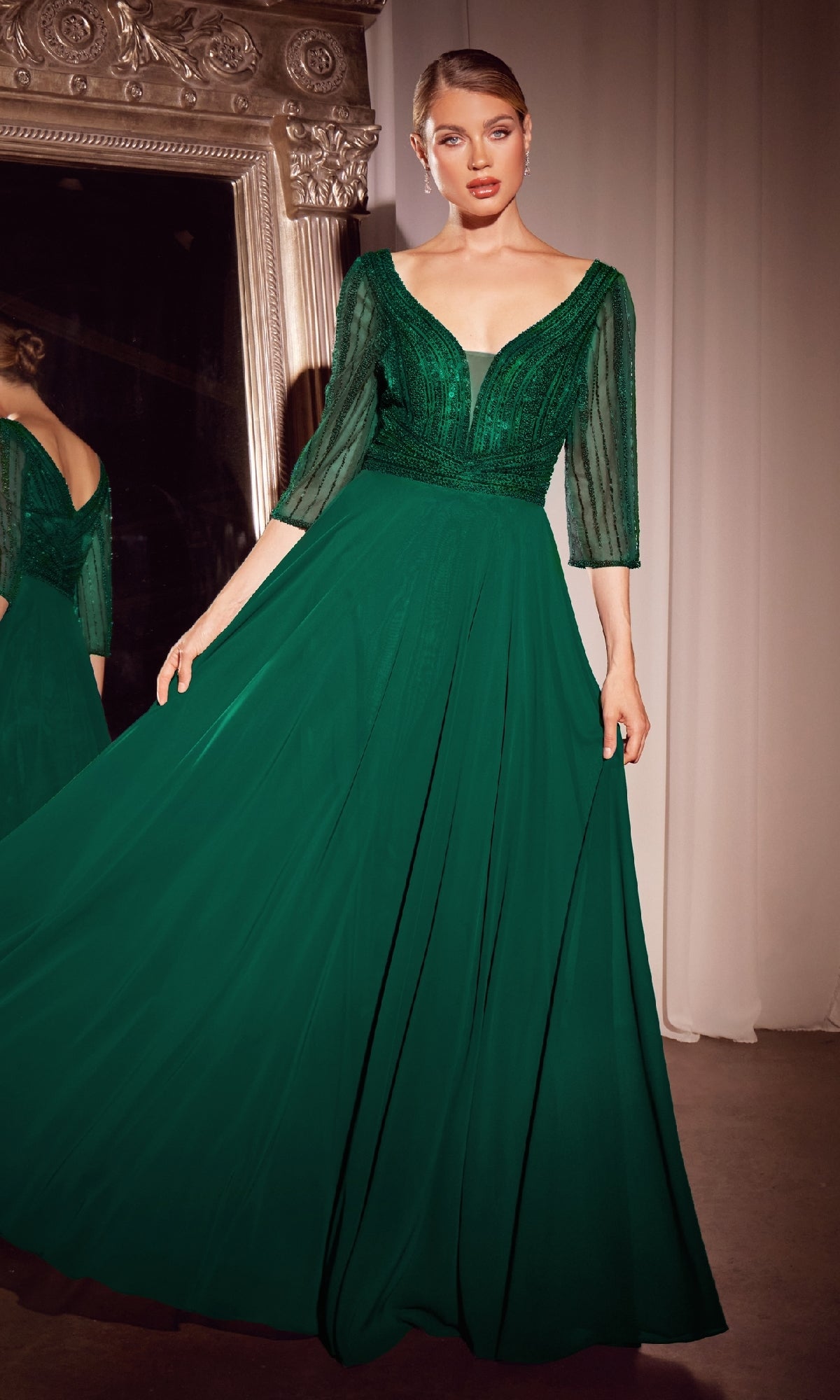 A woman stands indoors before a large ornate mirror, wearing the Ladivine CC446 Modest Long A-Line Formal Dress in emerald green with sheer three-quarter sleeves—a stunning choice for a mother of the bride gown.