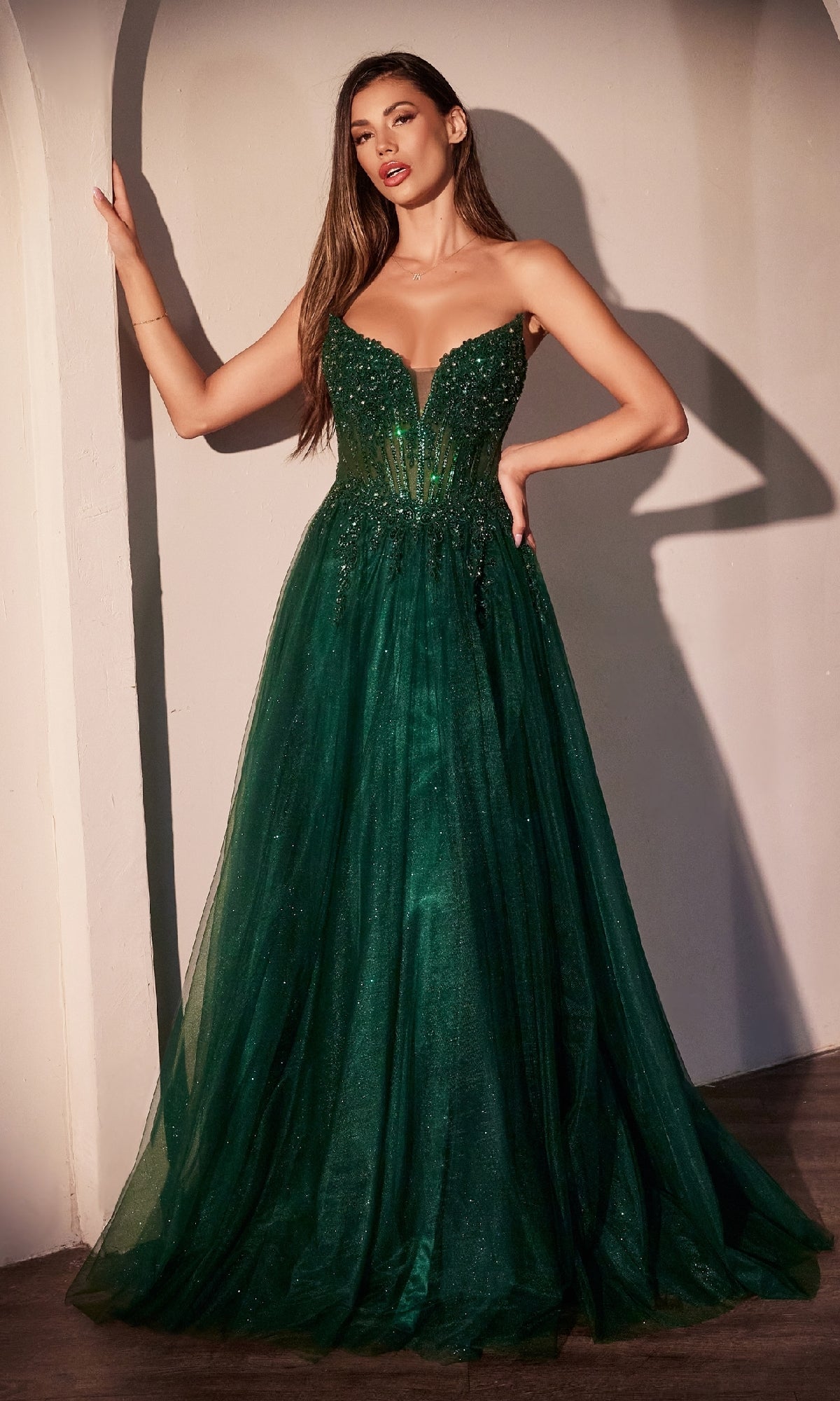 A woman in the Ladivine CC487 strapless long glitter prom dress, featuring a fitted sequined bodice and elegant A-line skirt, stands against a neutral wall as her shimmering evening gown drapes gracefully to the floor.