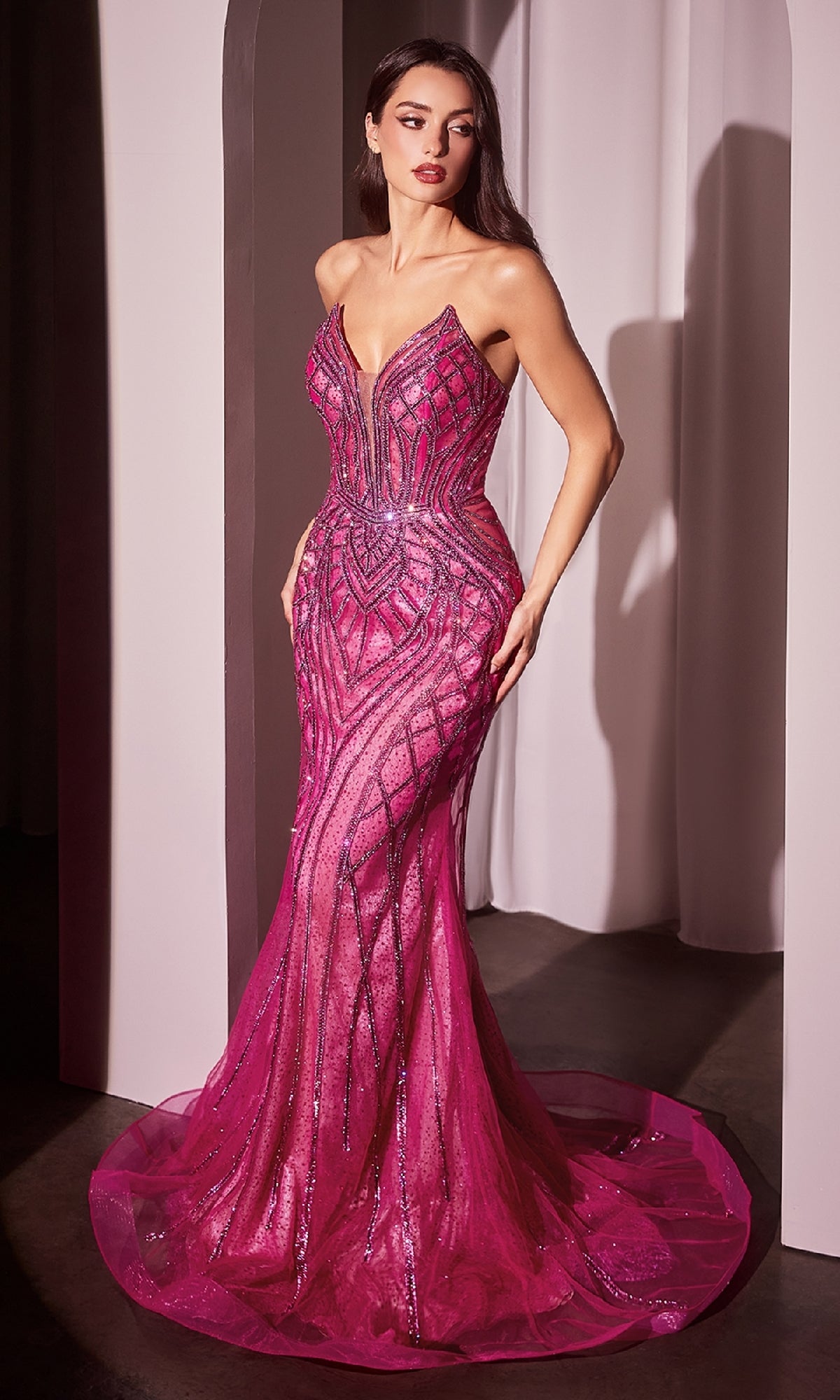 A woman in a Strapless Long Sequin-Print Prom Dress CC6018 in fuchsia, featuring a fitted, floor-length mermaid silhouette with geometric sequins, stands indoors near a white curtain.