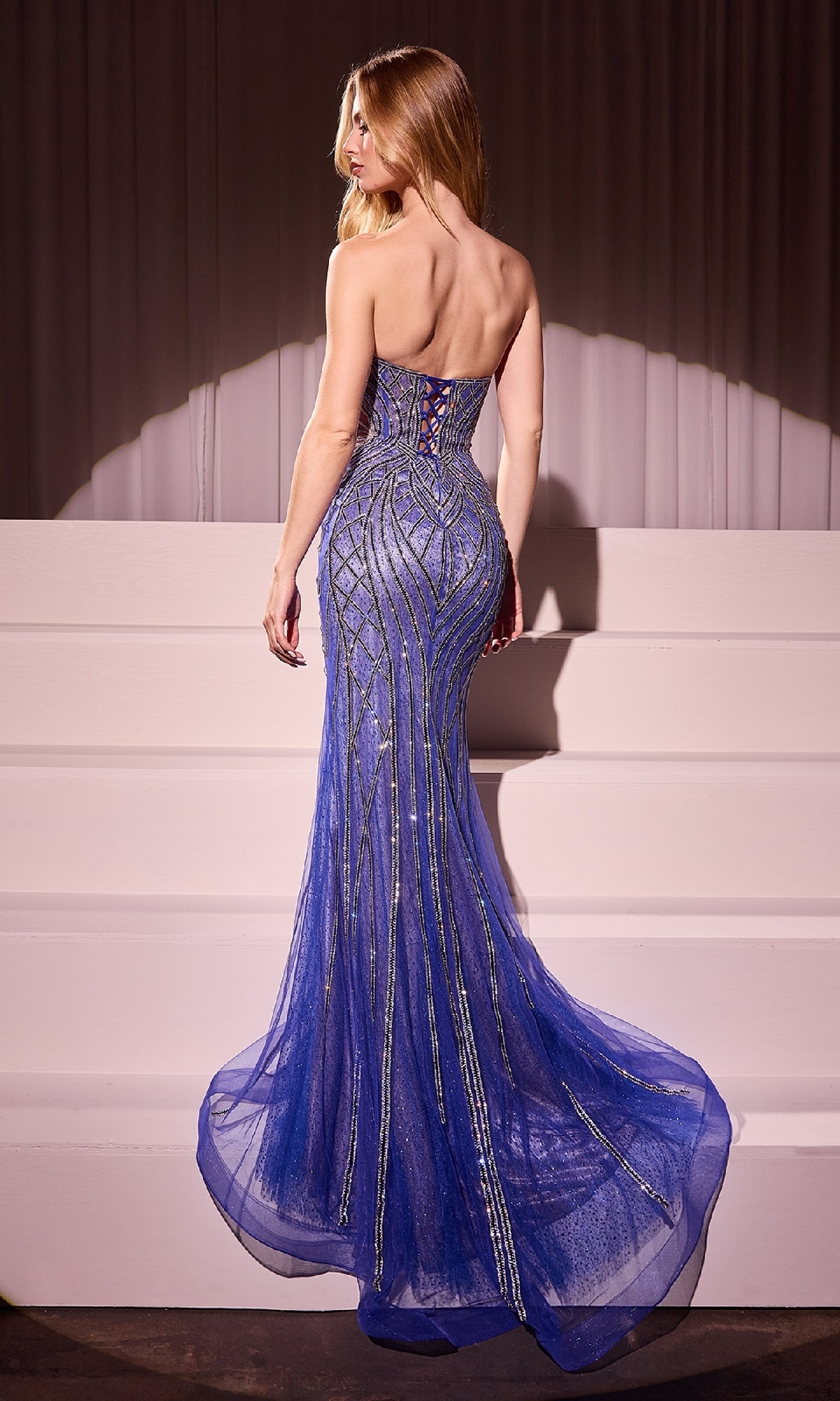 A woman in the Strapless Long Sequin-Print Prom Dress CC6018, designed with a mermaid silhouette and metallic sequin detailing, stands on white steps facing away from the camera.