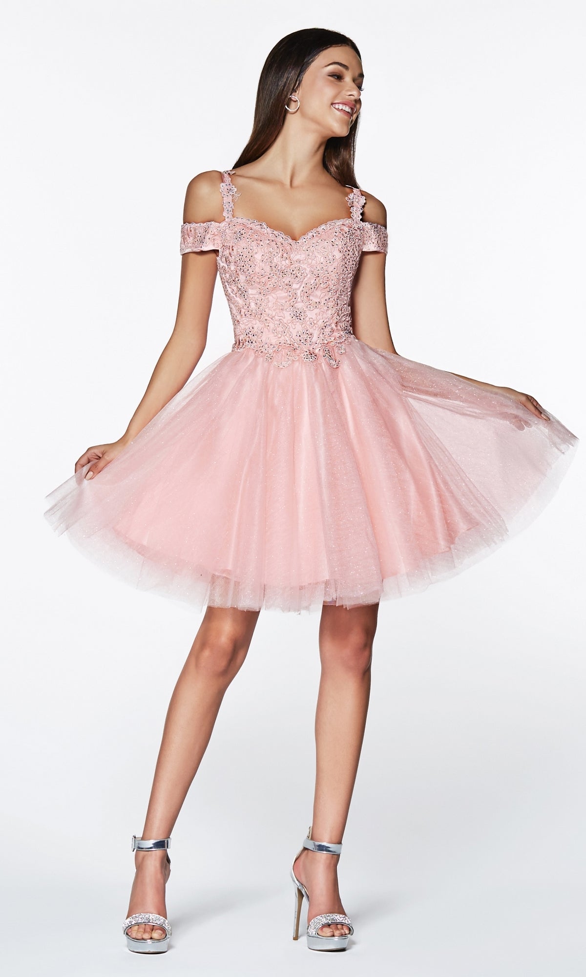 A woman wears the Cold-Shoulder Short Glitter Homecoming Dress CD0132, a light pink homecoming dress with lace and tulle details, paired with silver high-heeled sandals.