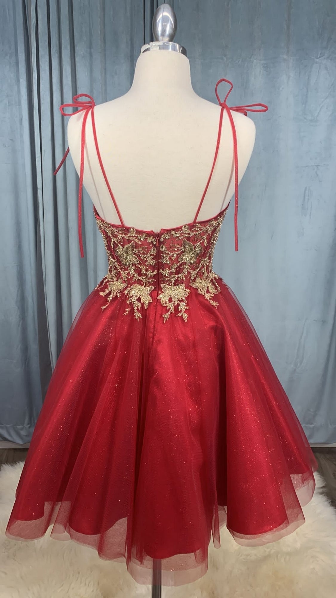 The Glitter-Tulle Short A-Line Prom Dress CD0188 is a red, knee-length dress with gold embroidered bodice, spaghetti straps tied at the shoulders, and a flared glitter tulle skirt, displayed on a dress form.