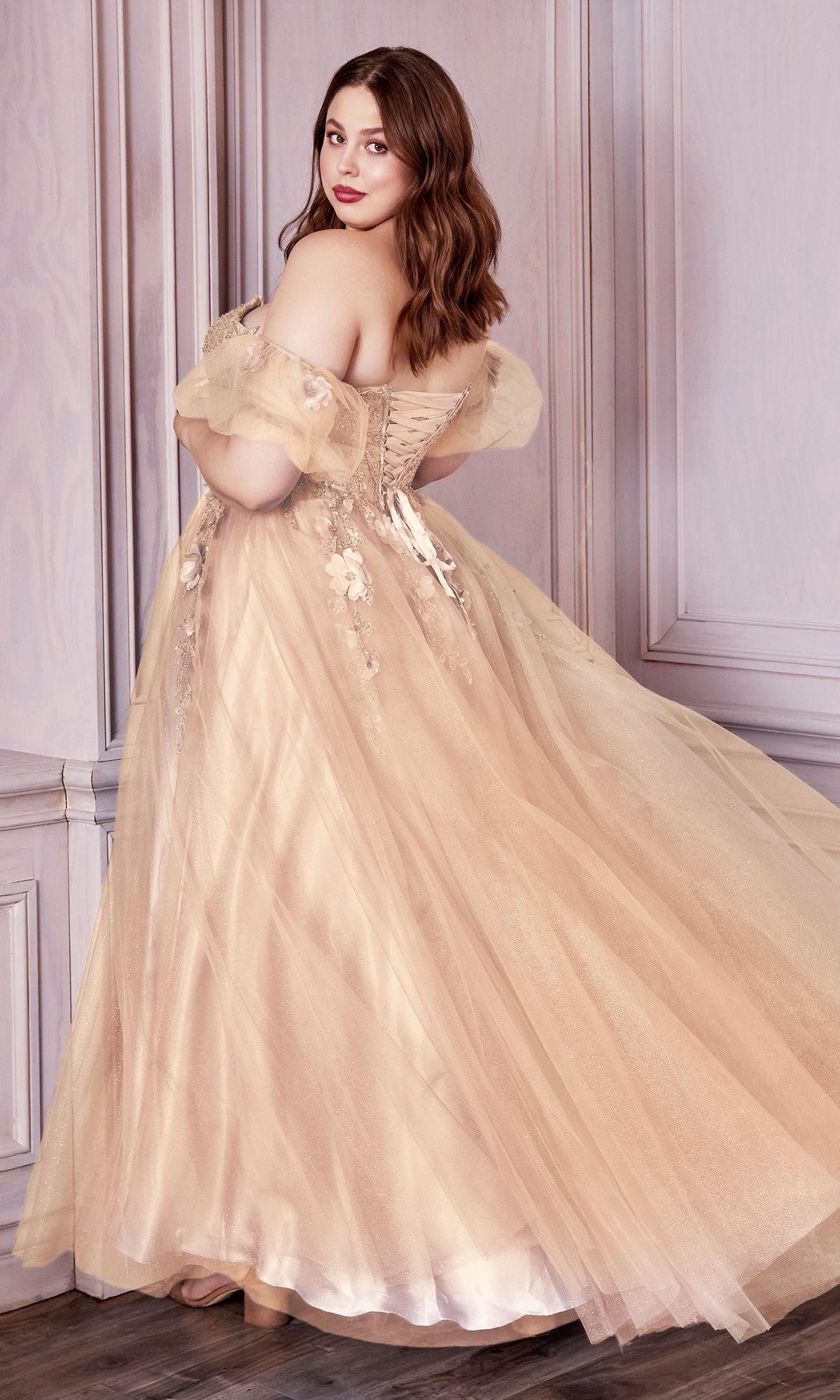 A woman in the Puff Sleeve Strapless Long Prom Dress CD0191, featuring a beige corset bodice and tulle skirt, stands in a wooden-paneled room, glancing over her shoulder.