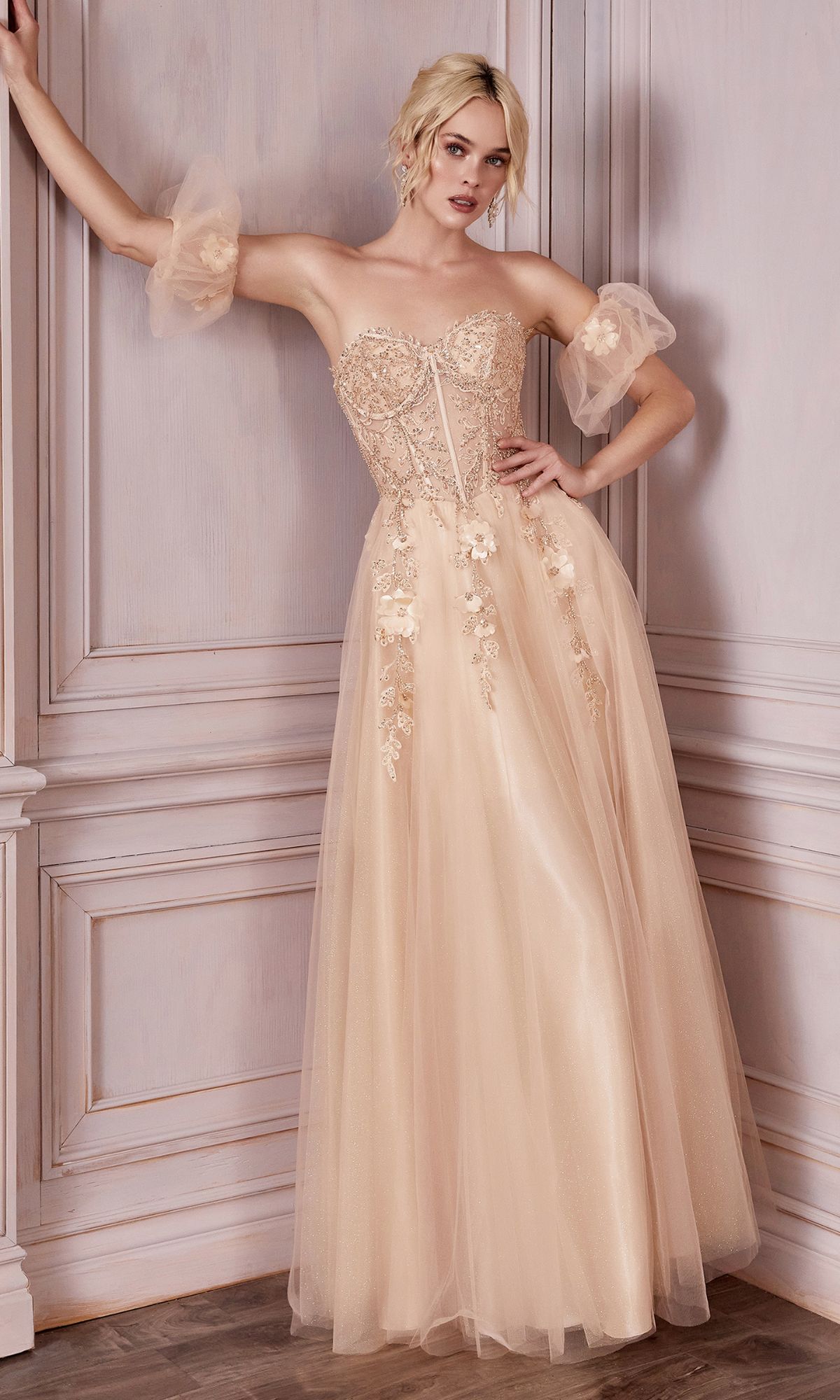 A woman stands against a decorative paneled wall wearing the Plus-Size Strapless Prom Ball Gown CD0191C in blush, featuring lace and floral appliqué details.