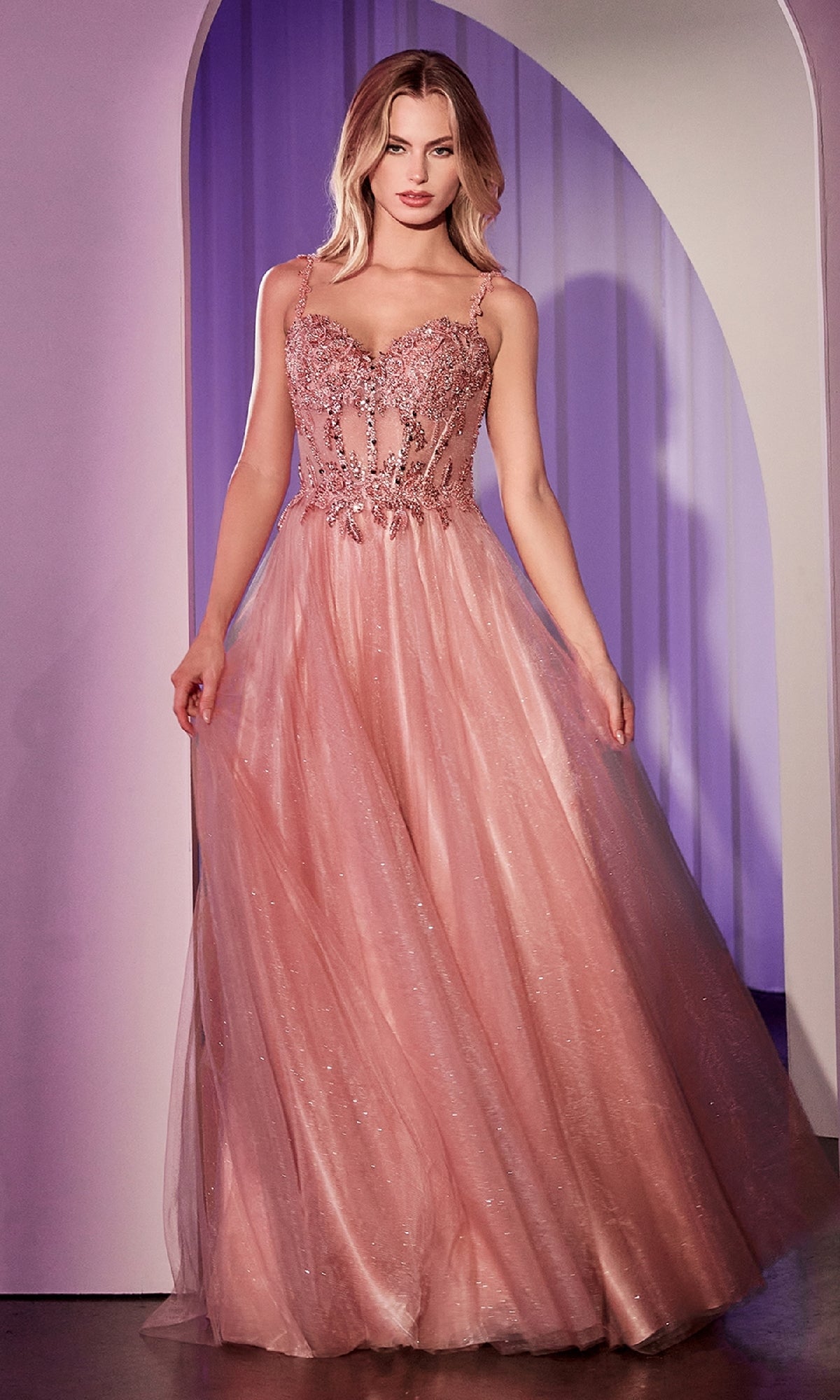 A woman stands in an archway wearing the Ladivine CD0234 Glitter-Tulle Long Prom Dress, a sleeveless blush pink gown with an embellished sweetheart bodice and a flowing tulle skirt.