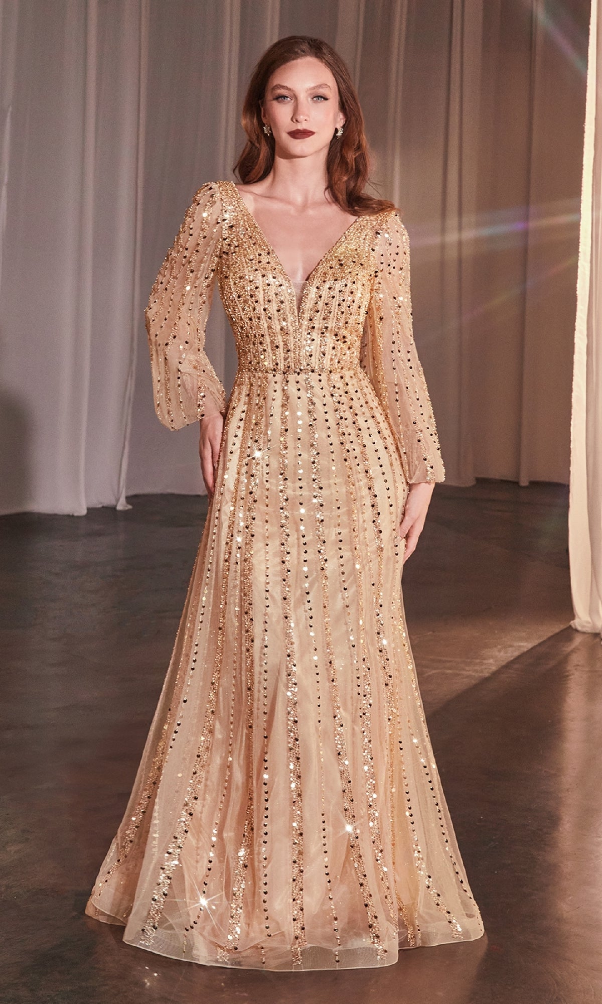 A woman stands indoors wearing the Ladivine CD0240, a long-sleeved, floor-length beaded formal dress with a deep V-neckline.