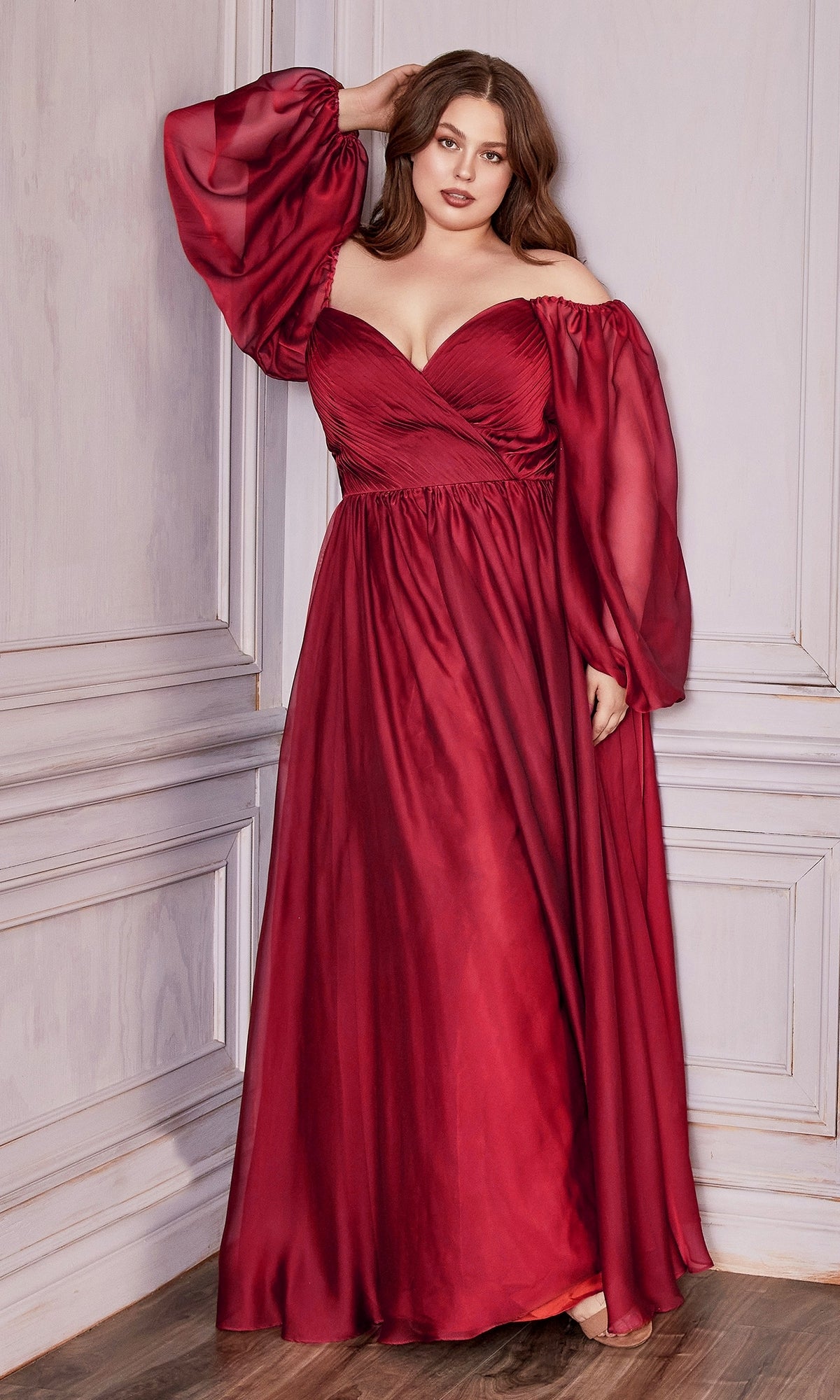 A woman stands indoors wearing the Ladivine Plus-Size Off-Shoulder Prom Dress CD243C in deep red, a floor-length gown with long sheer sleeves—an elegant and stunning choice for any formal evening.