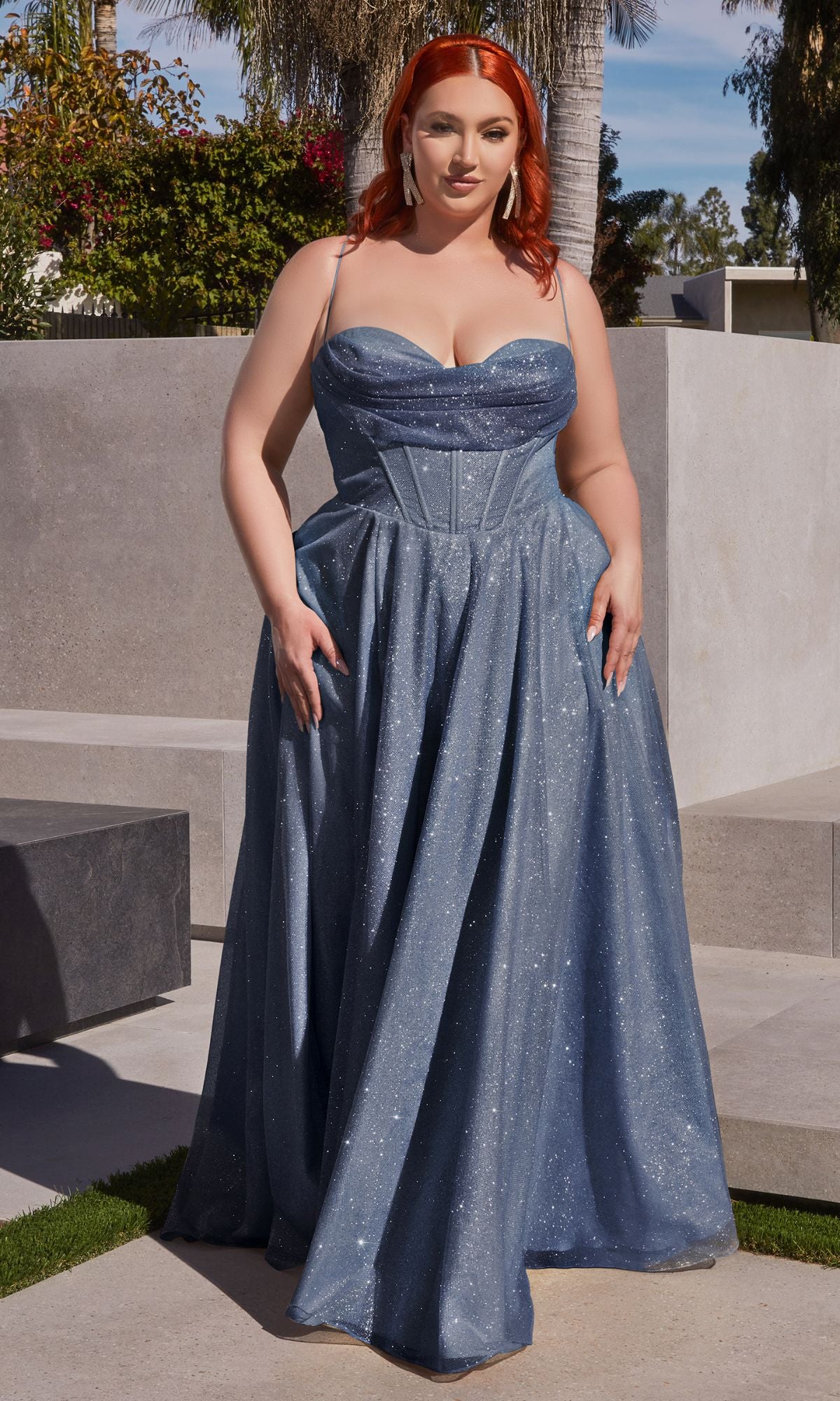 A red-haired woman wears the Plus-Size Long Glitter Prom Dress CD252C outdoors on a sunny day, standing near concrete steps with greenery in the background.
