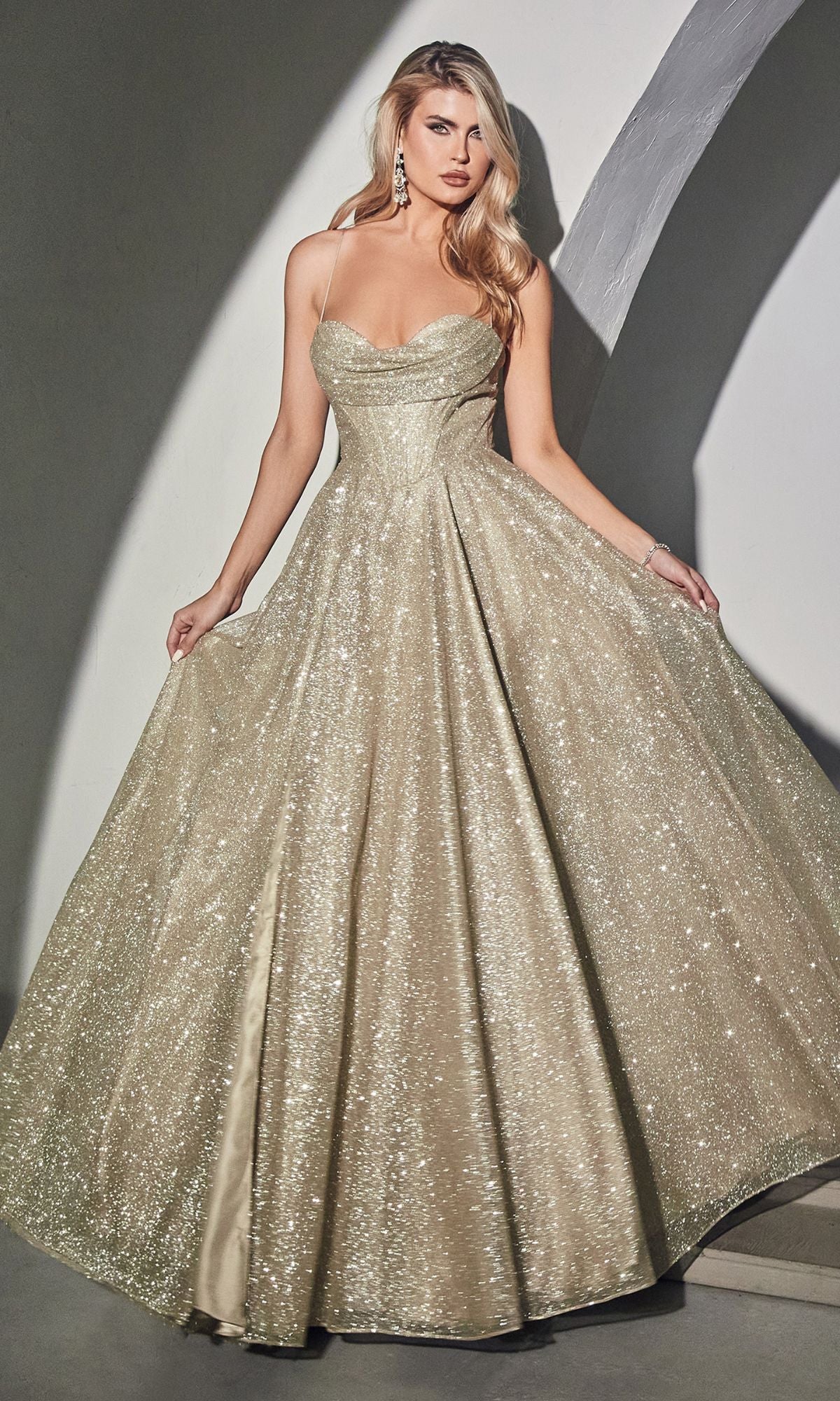 A woman wears the Draped-Bodice Long Glitter A-Line Prom Dress CD252—a shimmering gold gown with thin straps, a corset bodice, and a flared, floor-length skirt.