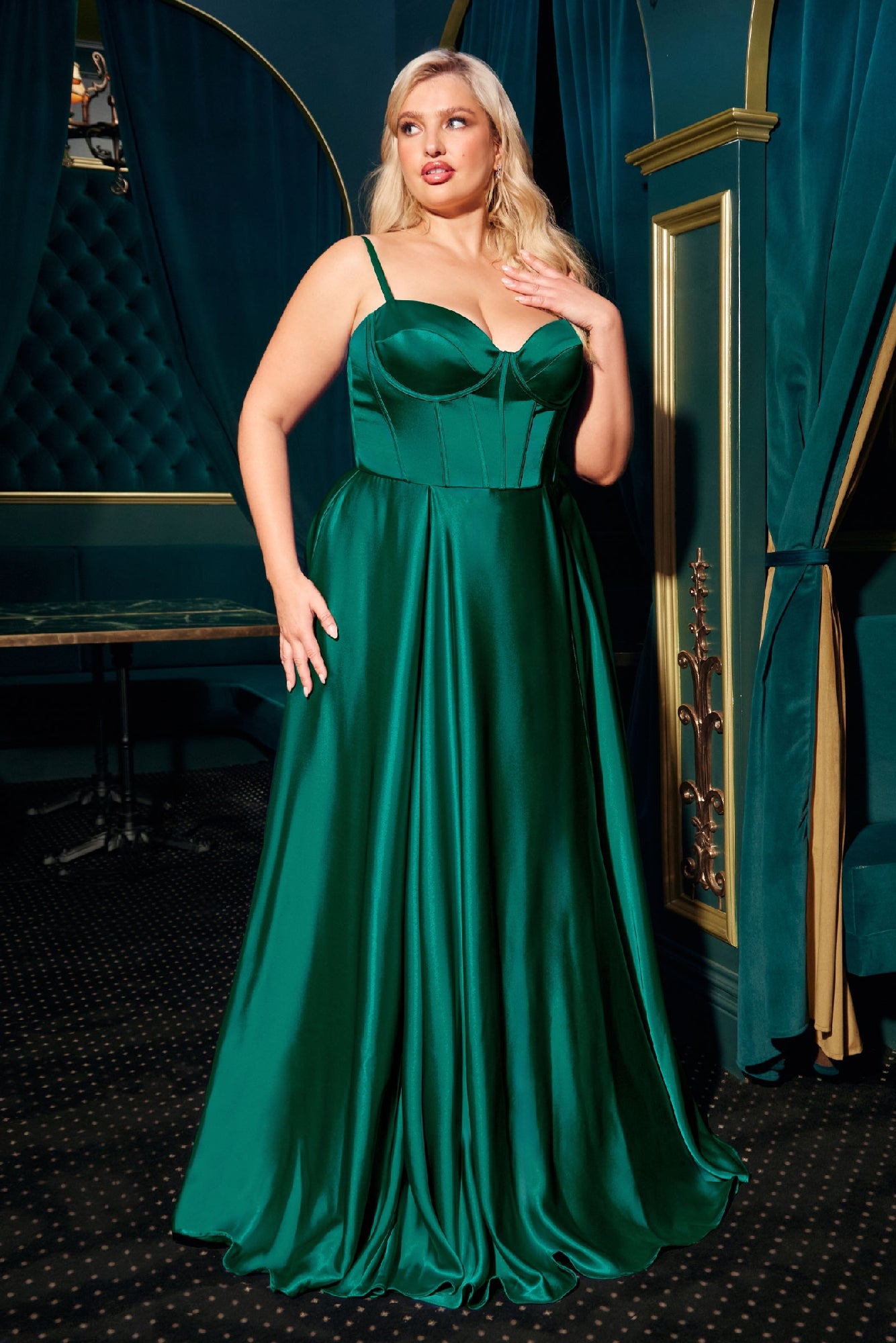 A woman poses gracefully indoors on a dark carpet, wearing the Ladivine CD337C plus-size long A-line emerald green prom dress with thin straps.