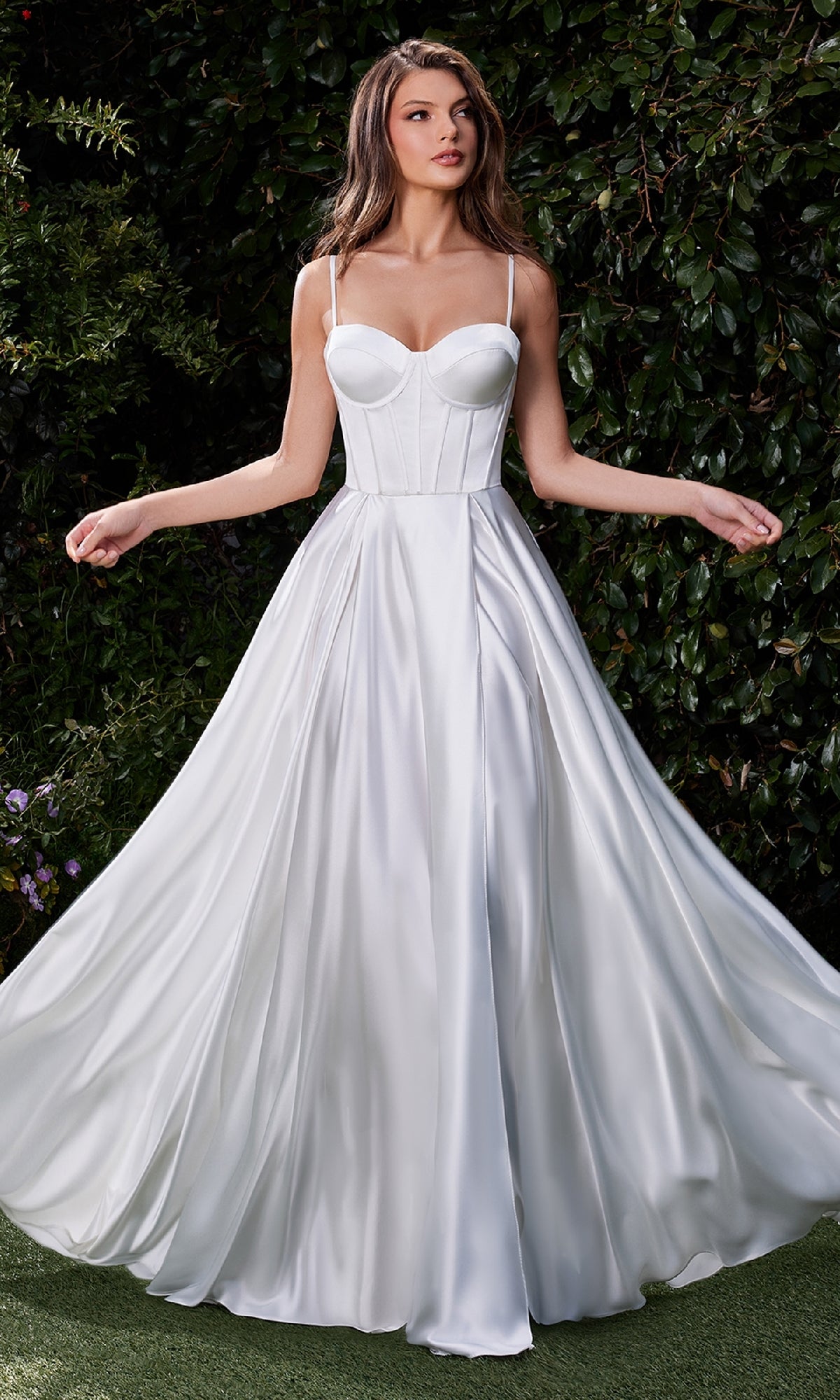 A woman stands outdoors in the Lace-Up Long White Prom Dress: Ladivine CD337W, featuring a corset bodice, thin straps, and a full flowing skirt; greenery is visible in the background.