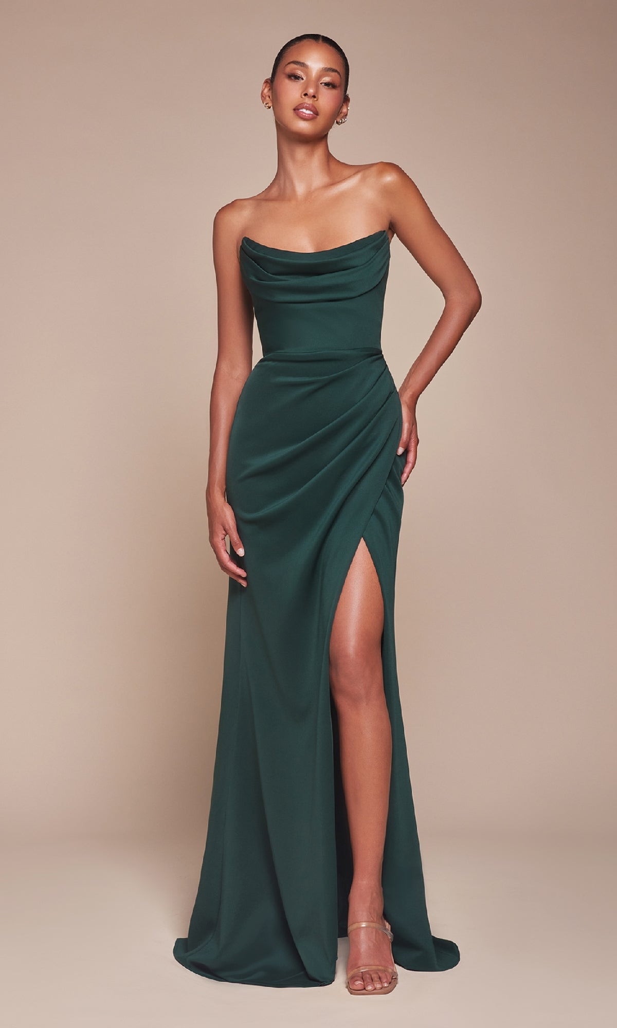 A woman wears the Ladivine CD355 Lace-Up Strapless Long Prom Gown in dark green with a draped bodice and high thigh slit, standing against a plain beige background.