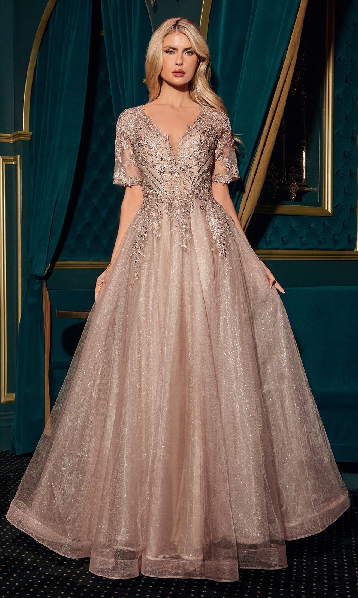 A woman stands before green curtains in a Ladivine CD726 Short-Sleeve Glitter Formal Dress, a floor-length, light pink gown with intricate beadwork and sheer short sleeves.