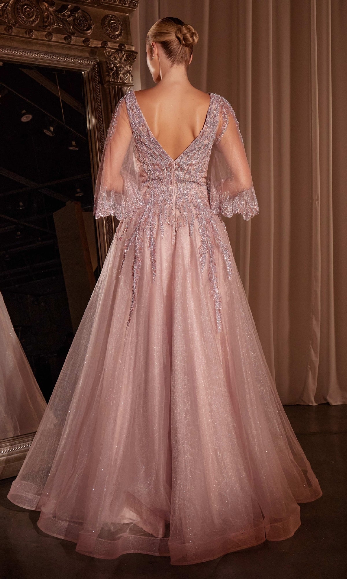 A woman with a neat bun wears the Bell-Sleeve Mauve Formal Dress: Ladivine CD784, standing gracefully in front of a large ornate mirror.
