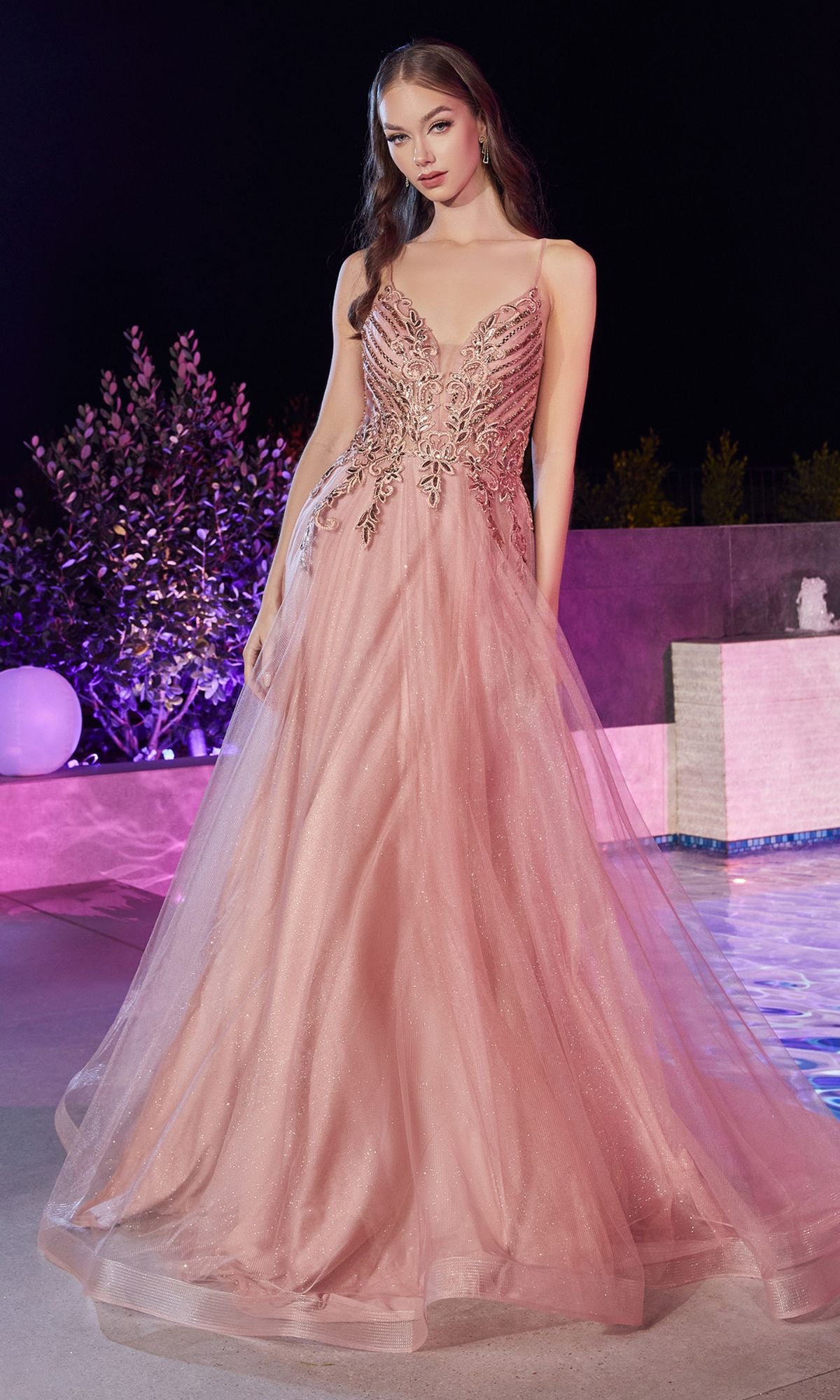 At night by a pool, a woman wears the Glitter-Bodice Long Prom Ball Gown CD874—a blush pink dress with a fitted, glittery bodice and thin straps.