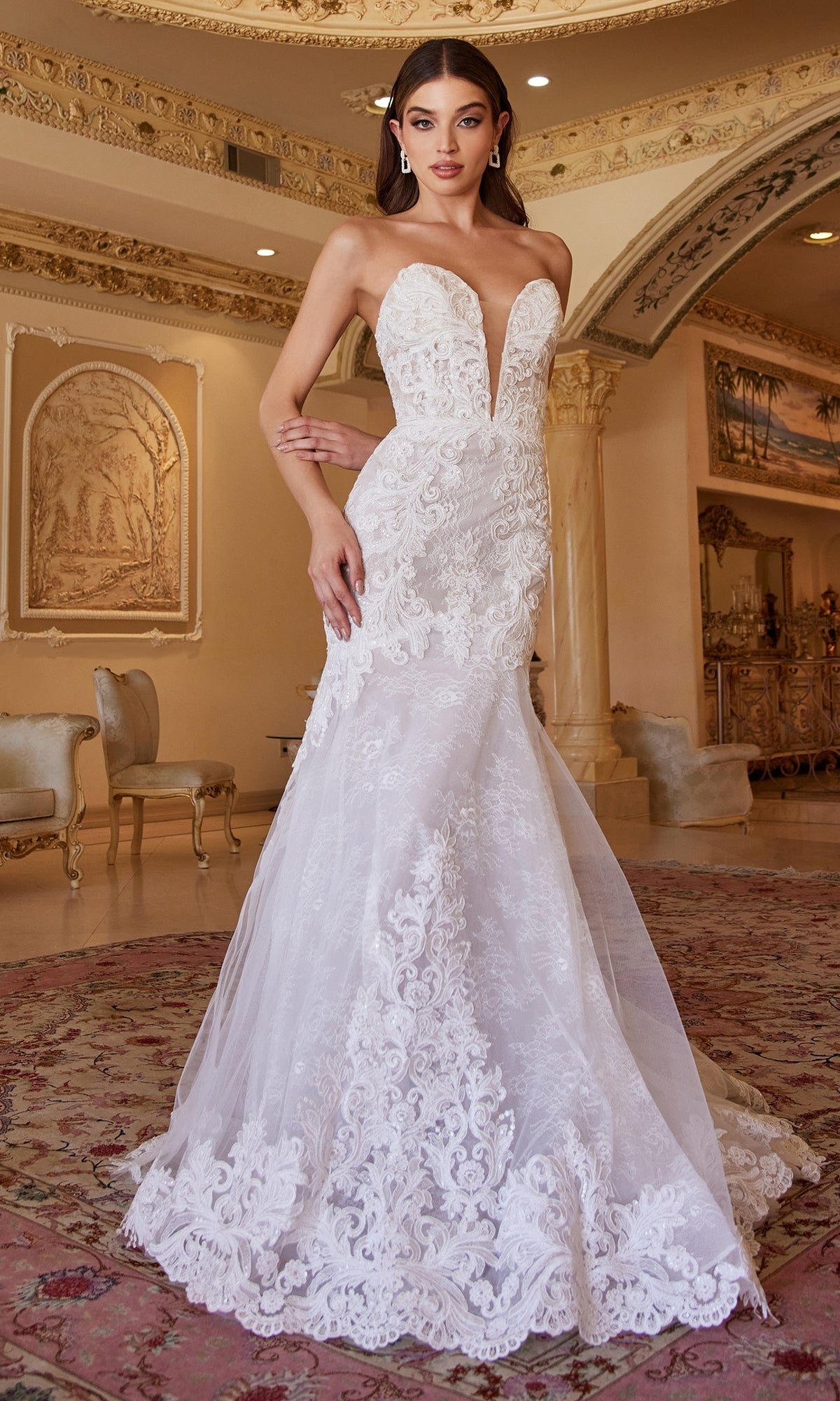 A woman in the Ladivine CD928 strapless mermaid wedding gown with lace and a plunging neckline stands in an elegant, classical room.