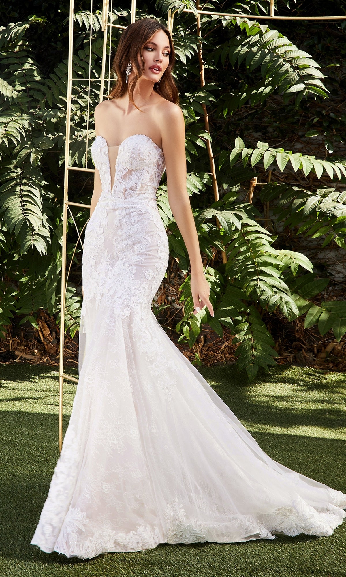 A woman in the Strapless Mermaid Wedding Gown: Ladivine CD928 stands on grass outdoors, with leafy green plants in the background.