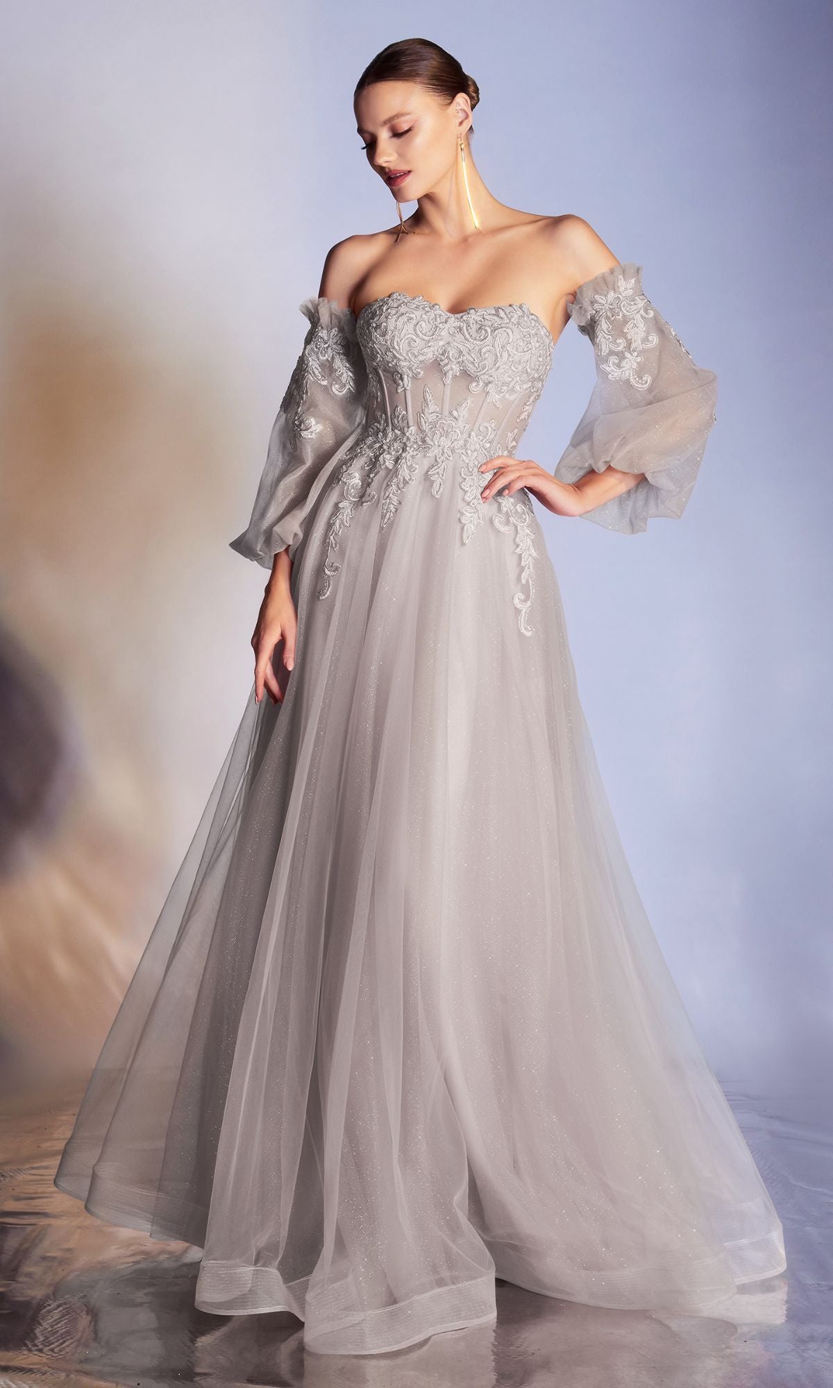A woman in the Strapless Puff-Sleeve Long Prom Dress CD948, featuring light gray tulle, sheer removable puff sleeves, and a flowing skirt, stands against a softly lit background.
