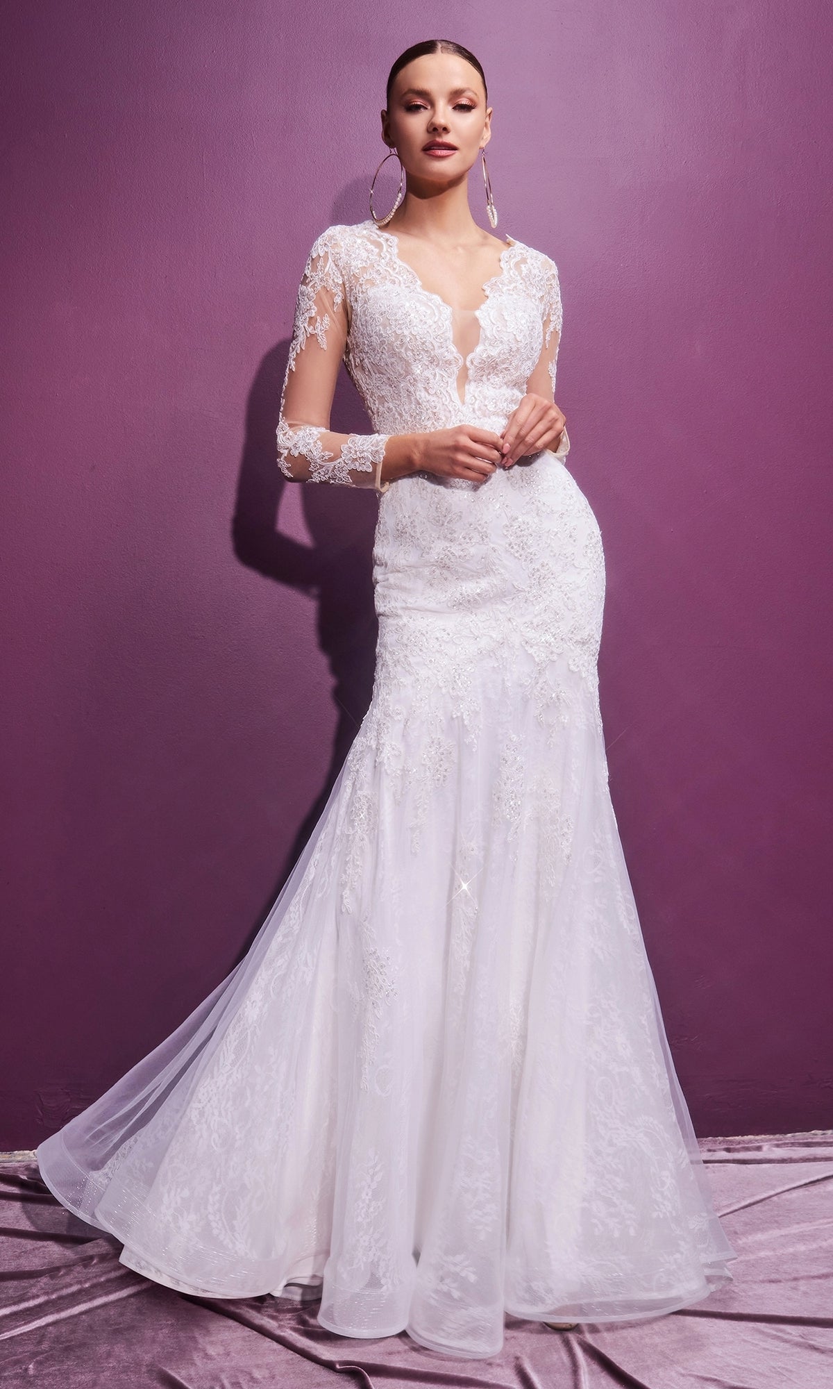 A woman stands against a purple wall wearing the Long Sleeve Long White Wedding Dress CD951W—an elegant, lace-embellished gown with a fitted bodice and flowing skirt.