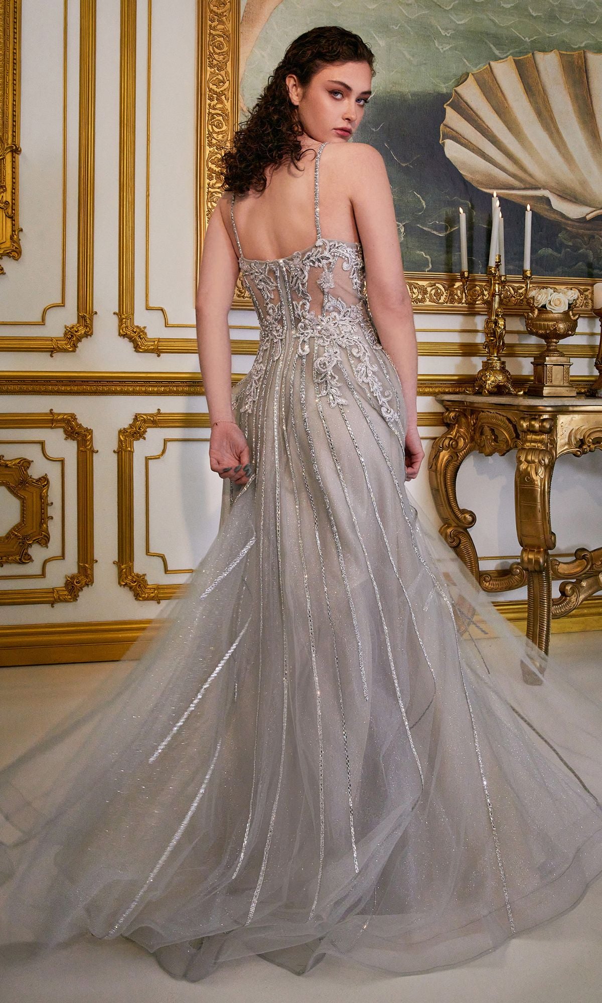 A woman in the Long A-Line Prom Dress with Sheer Bodice CD994 stands in an ornate, gold-trimmed room, showcasing the dress’s silver beading and sheer back as she faces away from the camera.