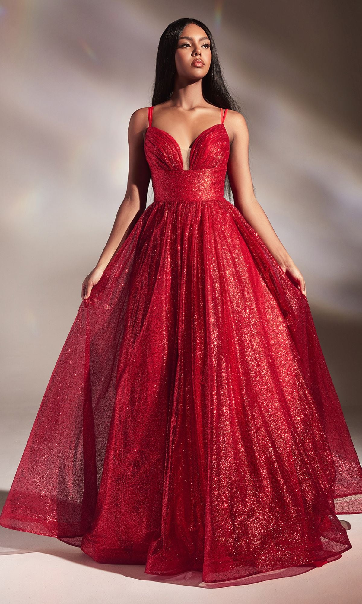 A woman in the Corset-Back Long Glitter Prom Ball Gown CD996, a sleeveless, floor-length red dress with a fitted bodice and flared skirt, stands against a neutral background.