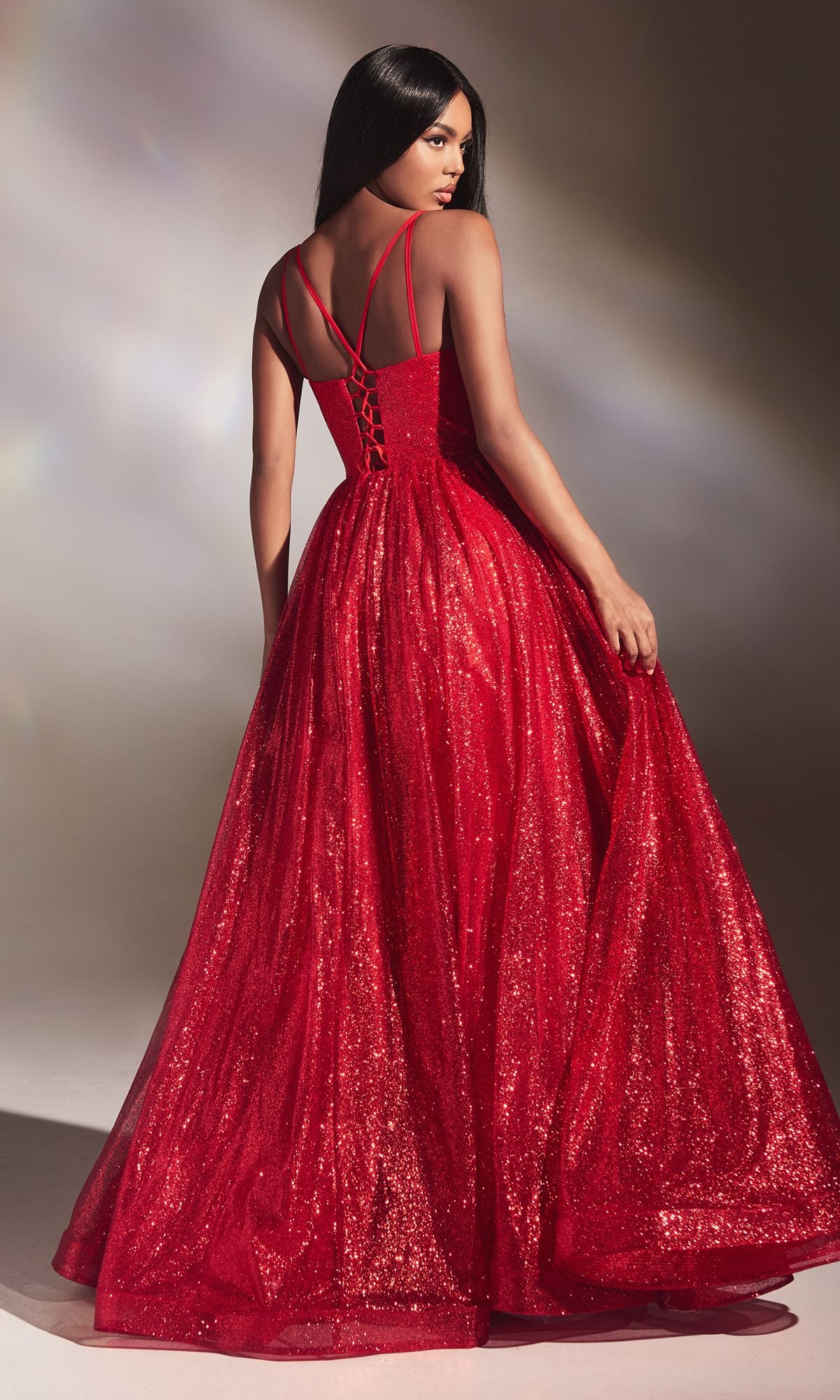 Woman wearing the Corset-Back Long Glitter Prom Ball Gown CD996, a floor-length red dress with a fitted bodice and sparkling details, posing with her back turned and gracefully holding the skirt.