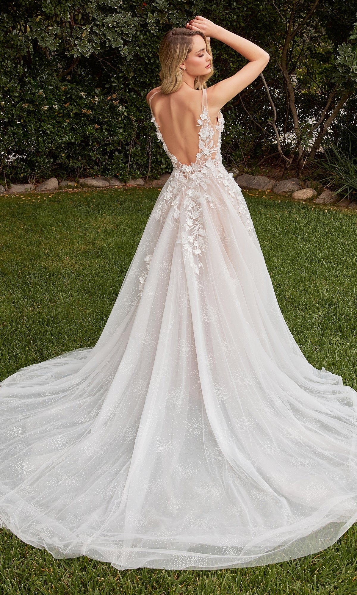 A woman stands on grass, framed by trees, wearing the Long Sleeve Long White Wedding Dress CDS436W featuring 3-D floral details and removable sleeves.