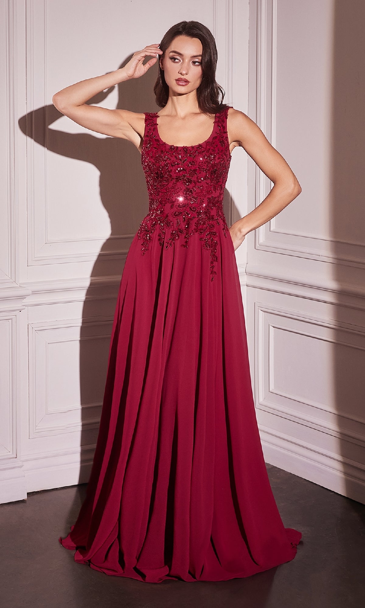 A woman stands indoors wearing the Beaded-Cape Long Formal Dress (CLCDS503)—a sleeveless, floor-length burgundy gown with floral embellishments on the bodice.