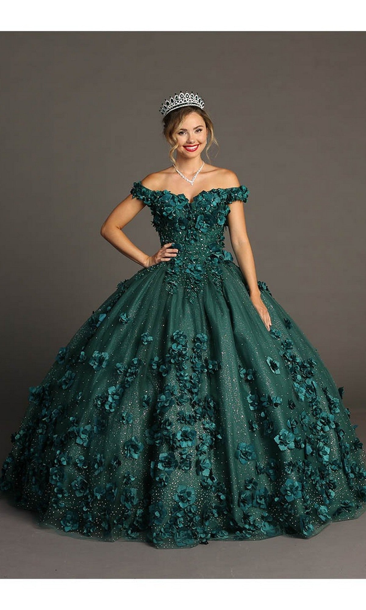 A woman wearing the Quinceanera Dress CHF3036 By Chicas in green—a dramatic off-the-shoulder ballgown featuring intricate 3D floral accents in tulle—accessorized with a tiara and necklace, stands against a plain background.