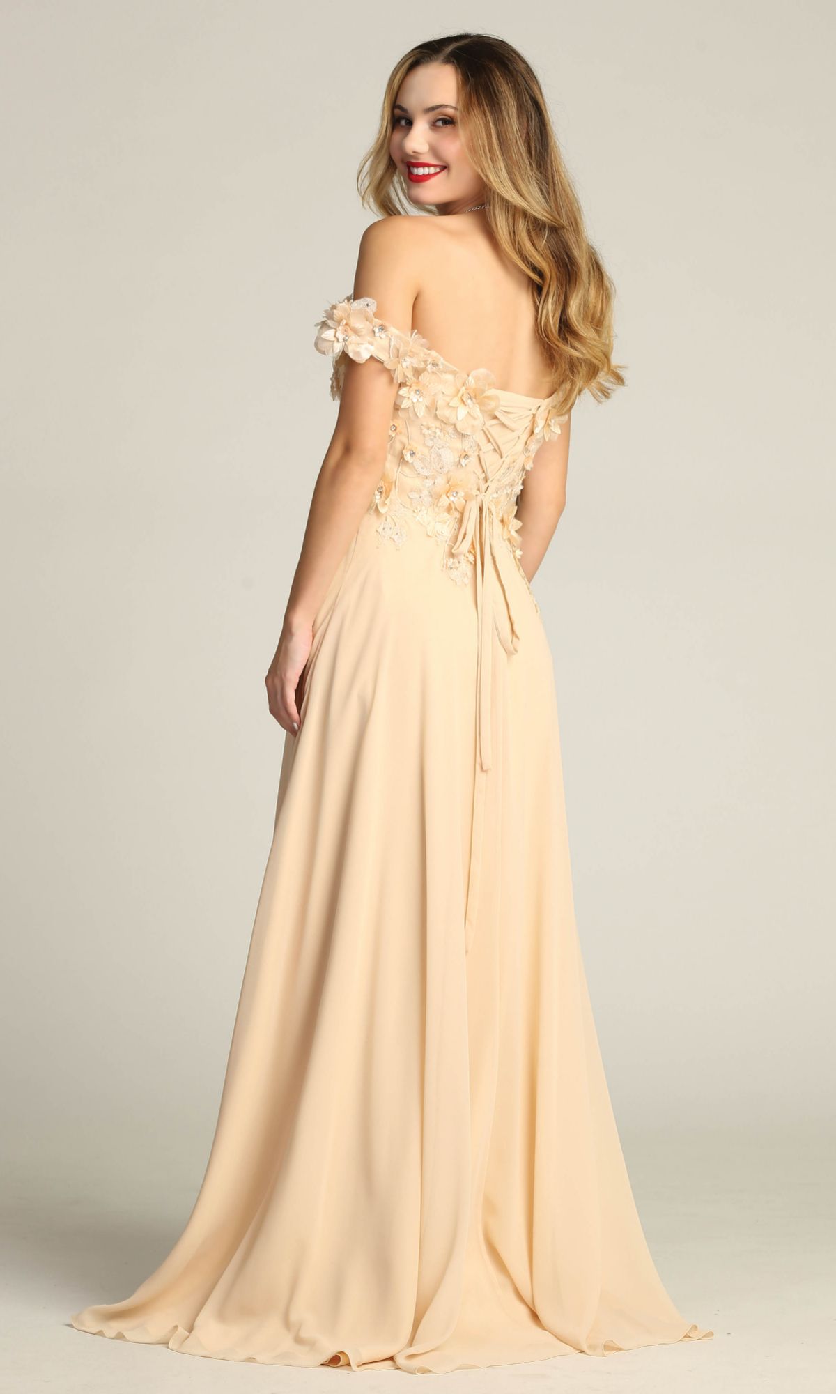 A woman stands gracefully, looking over her shoulder, in the Chicas CHF3059 Off-Shoulder Long A-Line Prom Dress, featuring light peach floral details and a lace-up back.