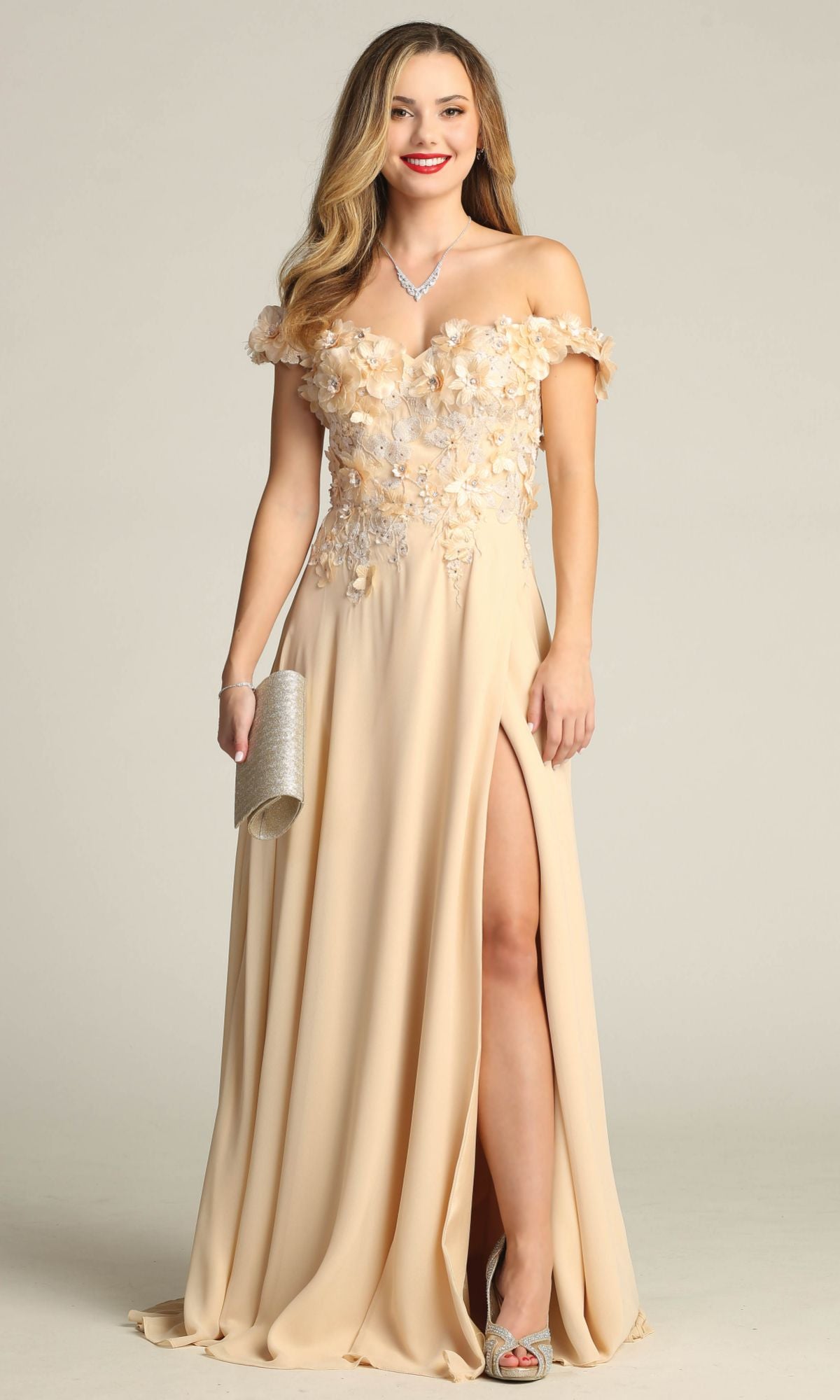 Wearing the Chicas CHF3059 off-shoulder long A-line prom dress, a woman in a light beige gown with floral embellishments and a thigh-high slit holds a silver clutch, complemented by silver heels and a necklace.