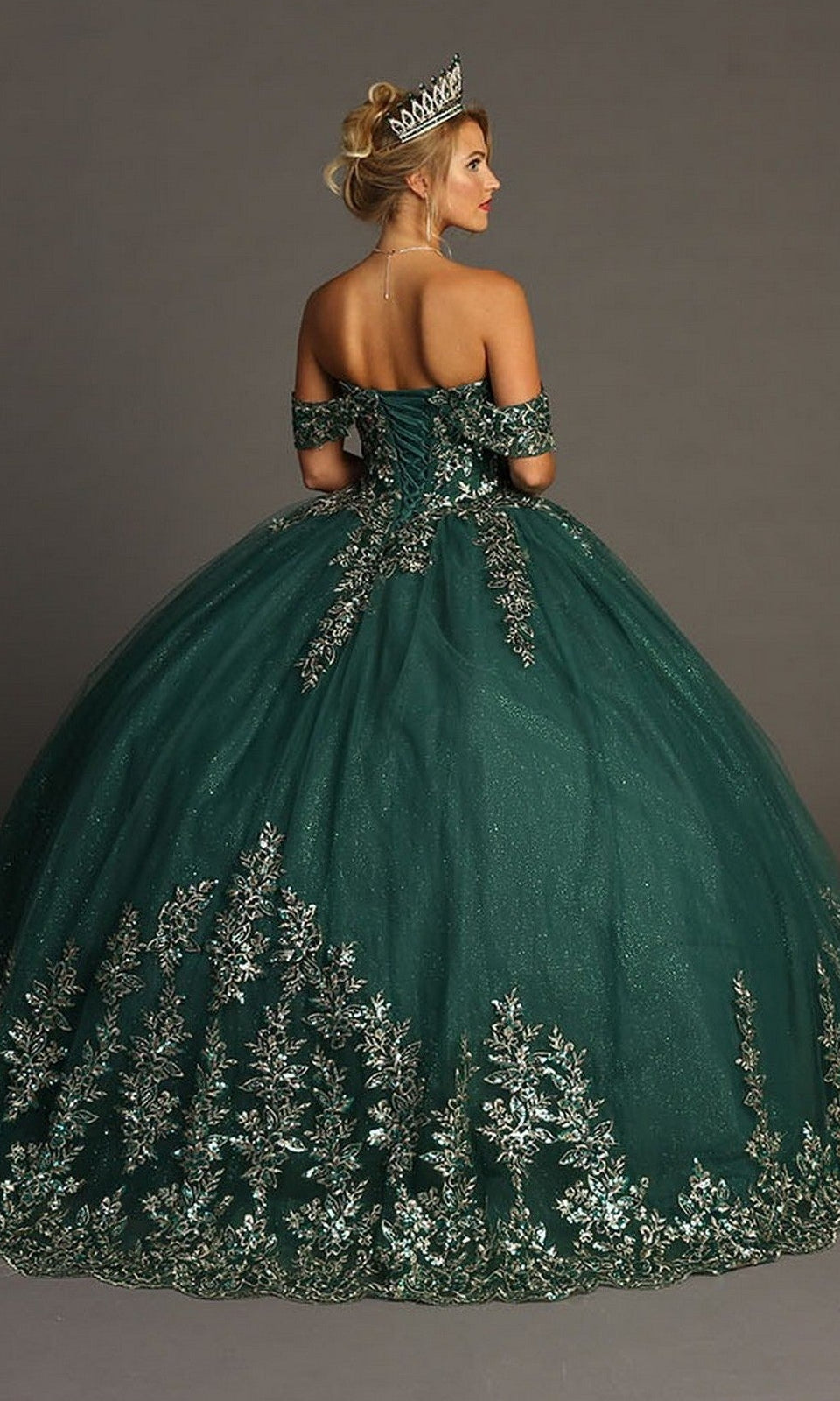 A woman wearing the Quinceanera Dress CHF3081 by Chicas—a dark green ballgown adorned with intricate silver embroidery and paired with a tiara—stands against a plain background, showcasing the perfect dress for an unforgettable celebration.