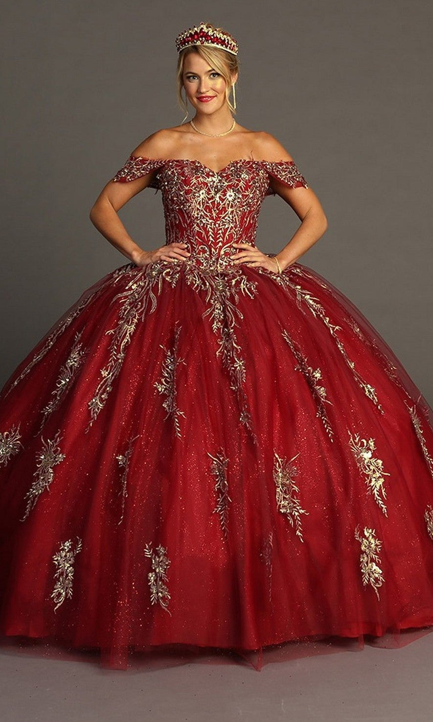A woman wearing the Quinceanera Dress CHF3084 By Chicas in rich red with gold floral embroidery and a matching crown, standing against a plain gray background.