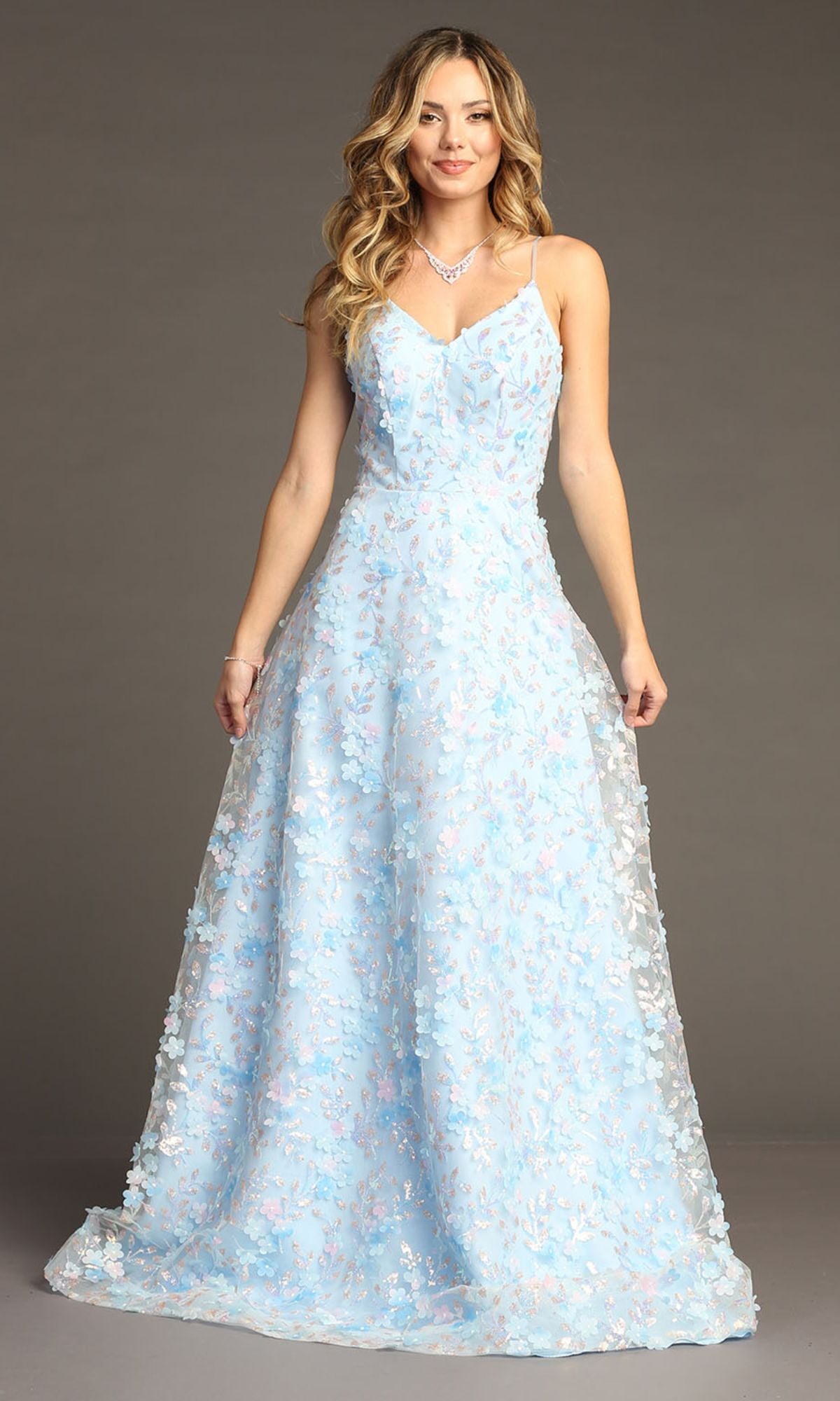 A woman stands in front of a plain background wearing the Chicas CHF3092, a long light blue prom dress with spaghetti straps and delicate 3-D floral details.