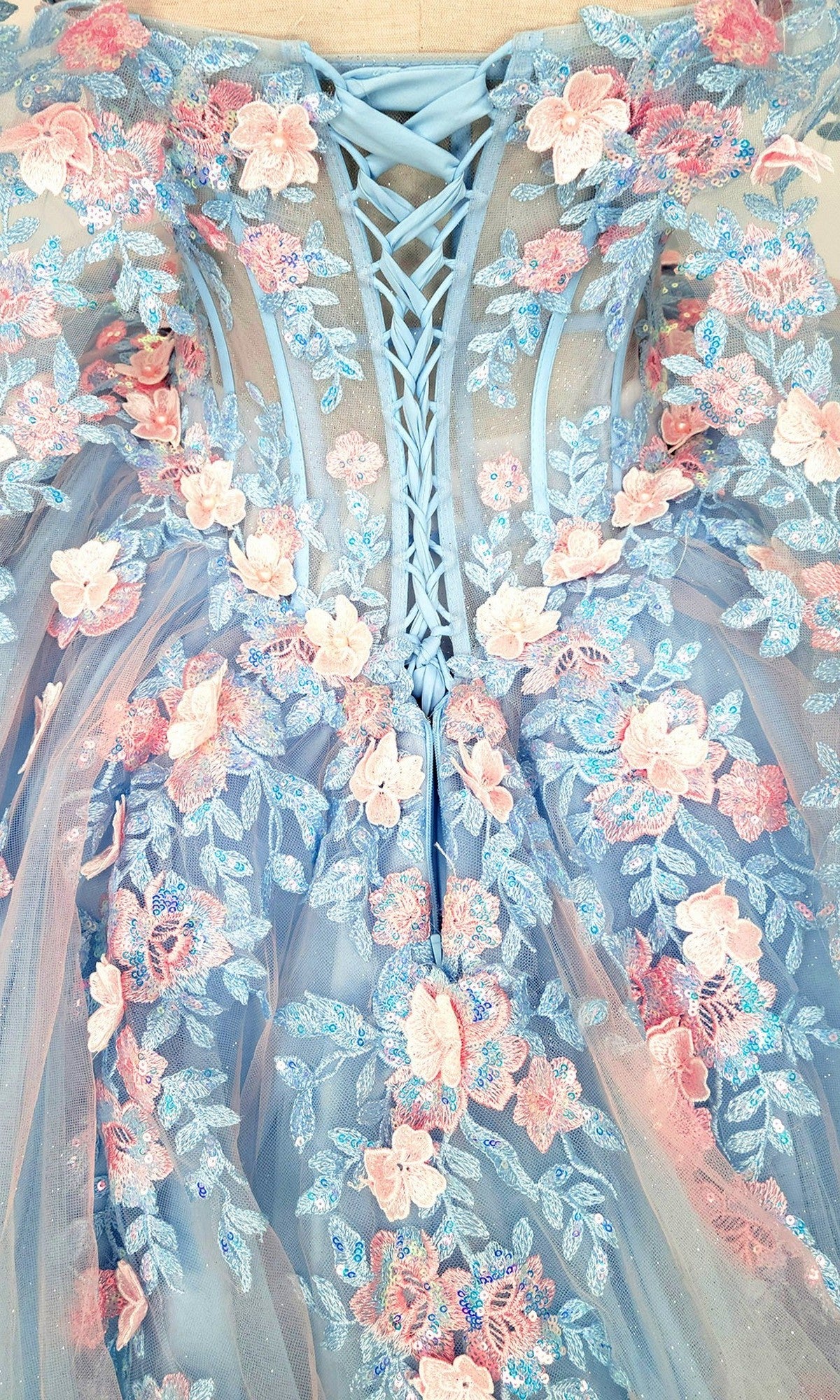 Close-up of the Quinceanera Dress CHF3117 By Chicas featuring a blue lace-up bodice embellished with delicate pink and blue 3D floral appliques and sheer tulle fabricโideal for a magical quinceanera or an enchanting tulle ballgown ensemble.