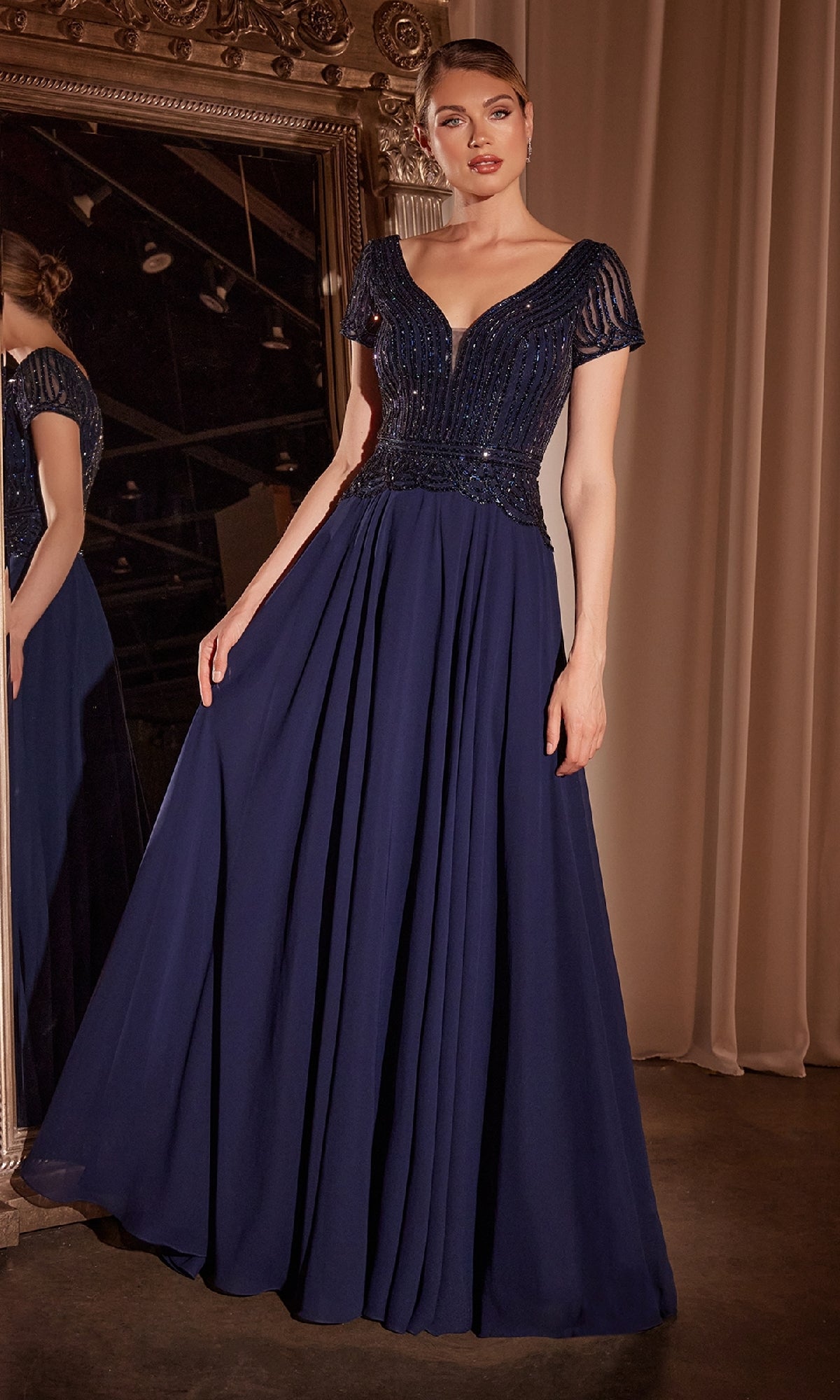 A woman stands before a mirror wearing the Ladivine CL07, a long flowy navy formal dress with short sleeves, an embellished bodice, and an A-line skirt.