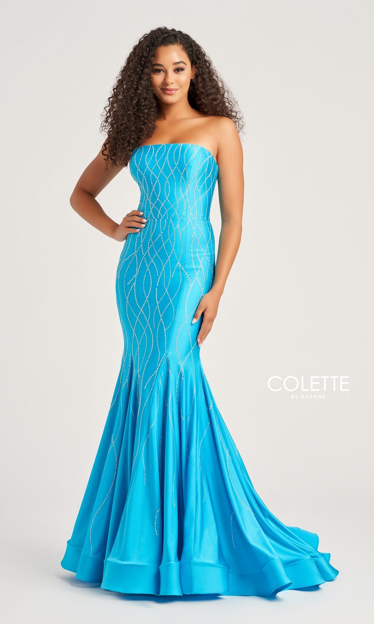 A woman poses confidently in the Colette Strapless Long Glitter Prom Dress CL5106—a fitted, bright blue mermaid gown with silver glitter print. One hand rests on her hip against a plain background, with
